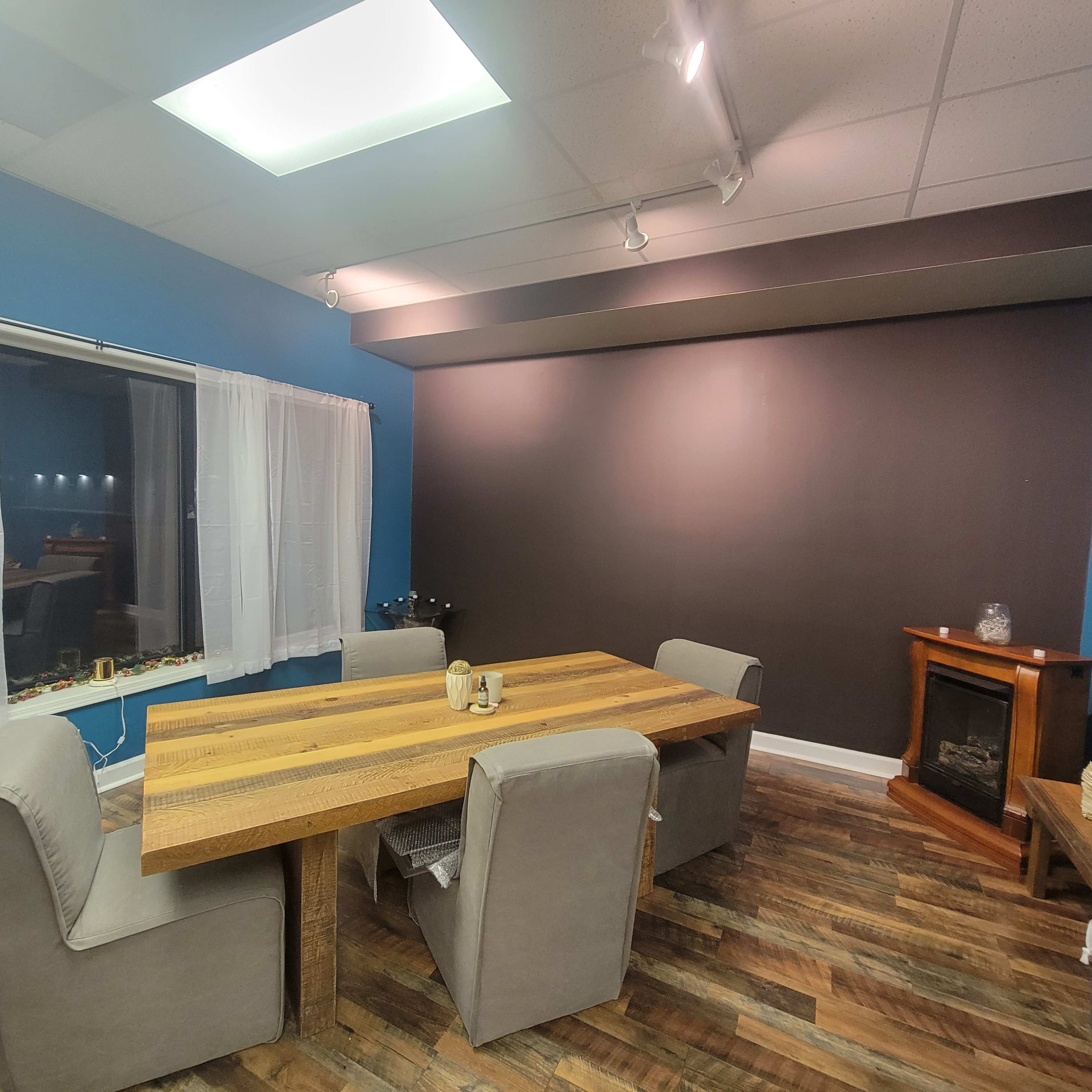A modern room with a wooden dining table surrounded by upholstered chairs, a cozy fireplace in the corner, and a large window with sheer curtains.