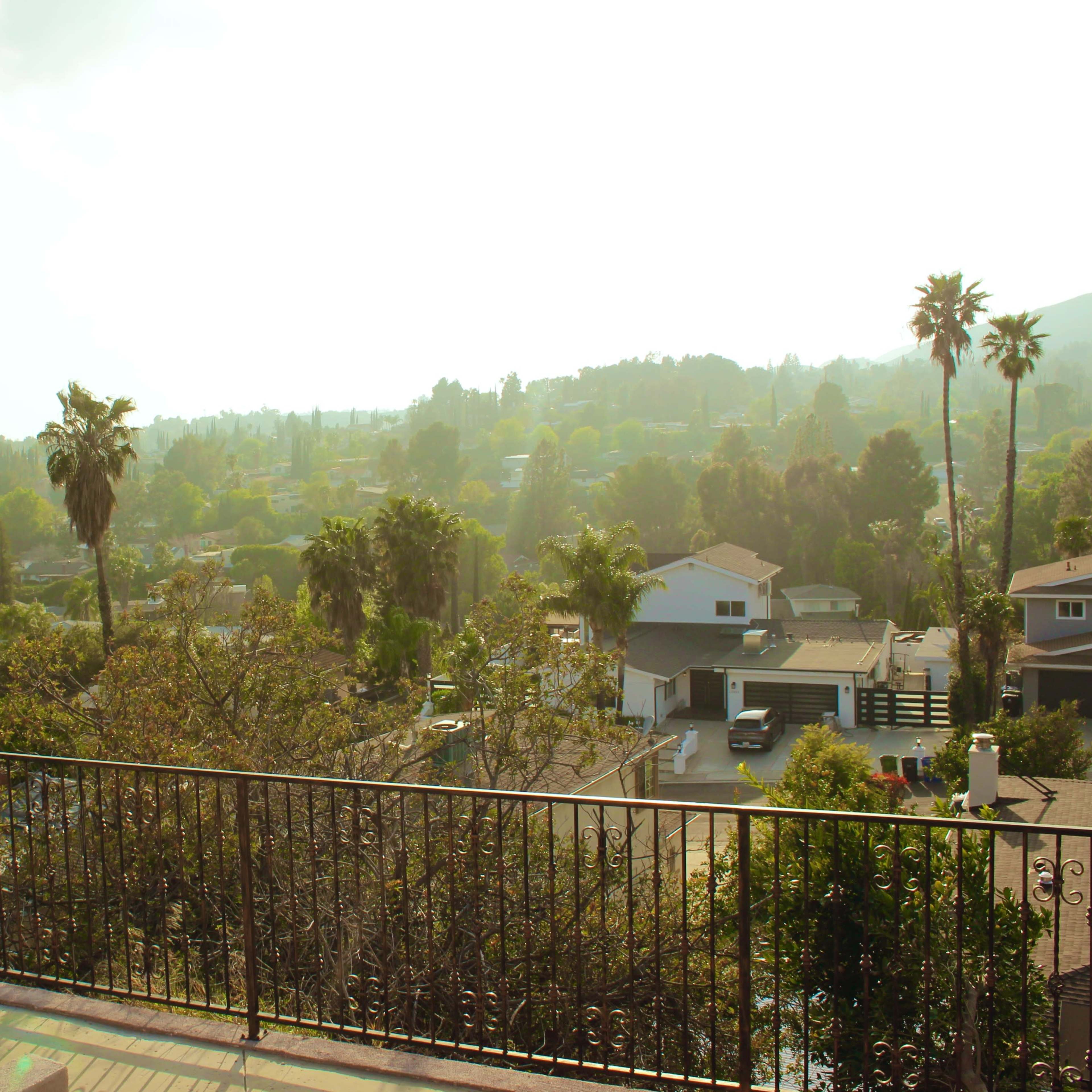 A clear view of a suburban landscape featuring houses, palm trees, and rolling hills under a bright sky.