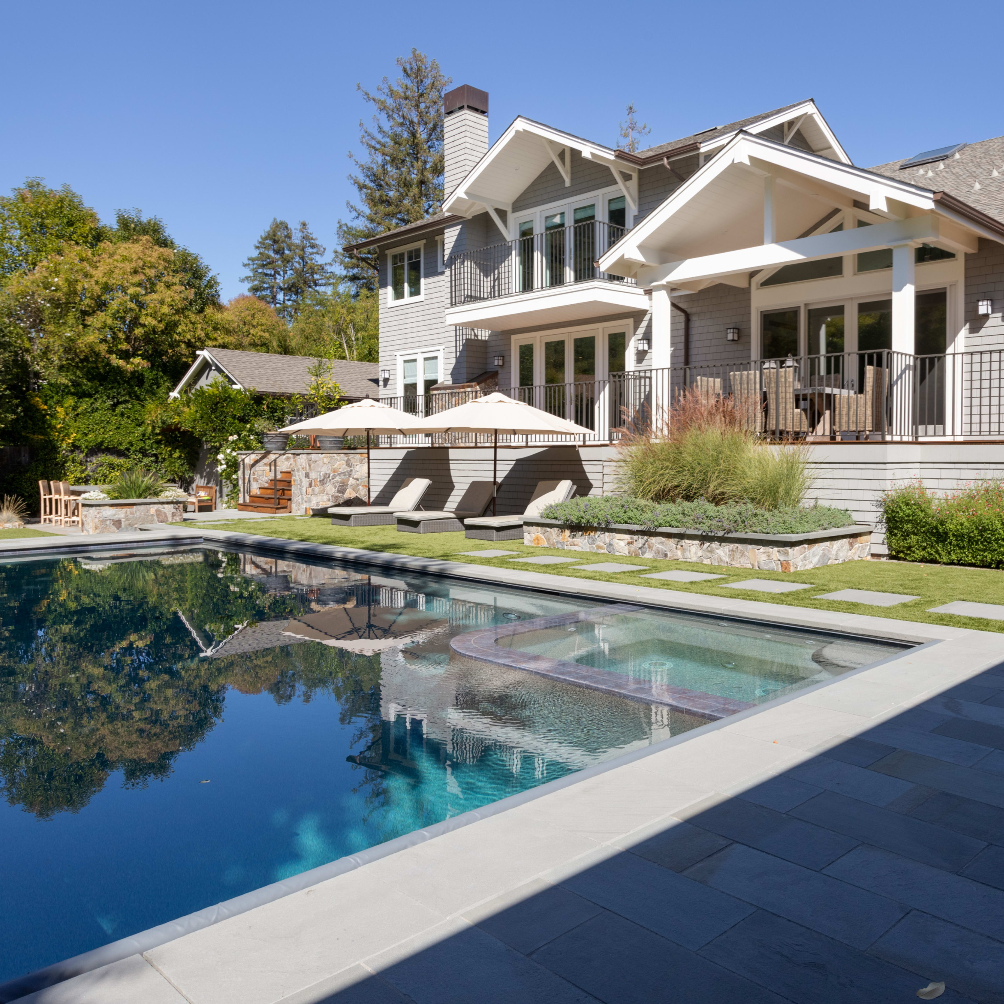 A modern house with a backyard pool is surrounded by landscaped greenery and outdoor furniture.