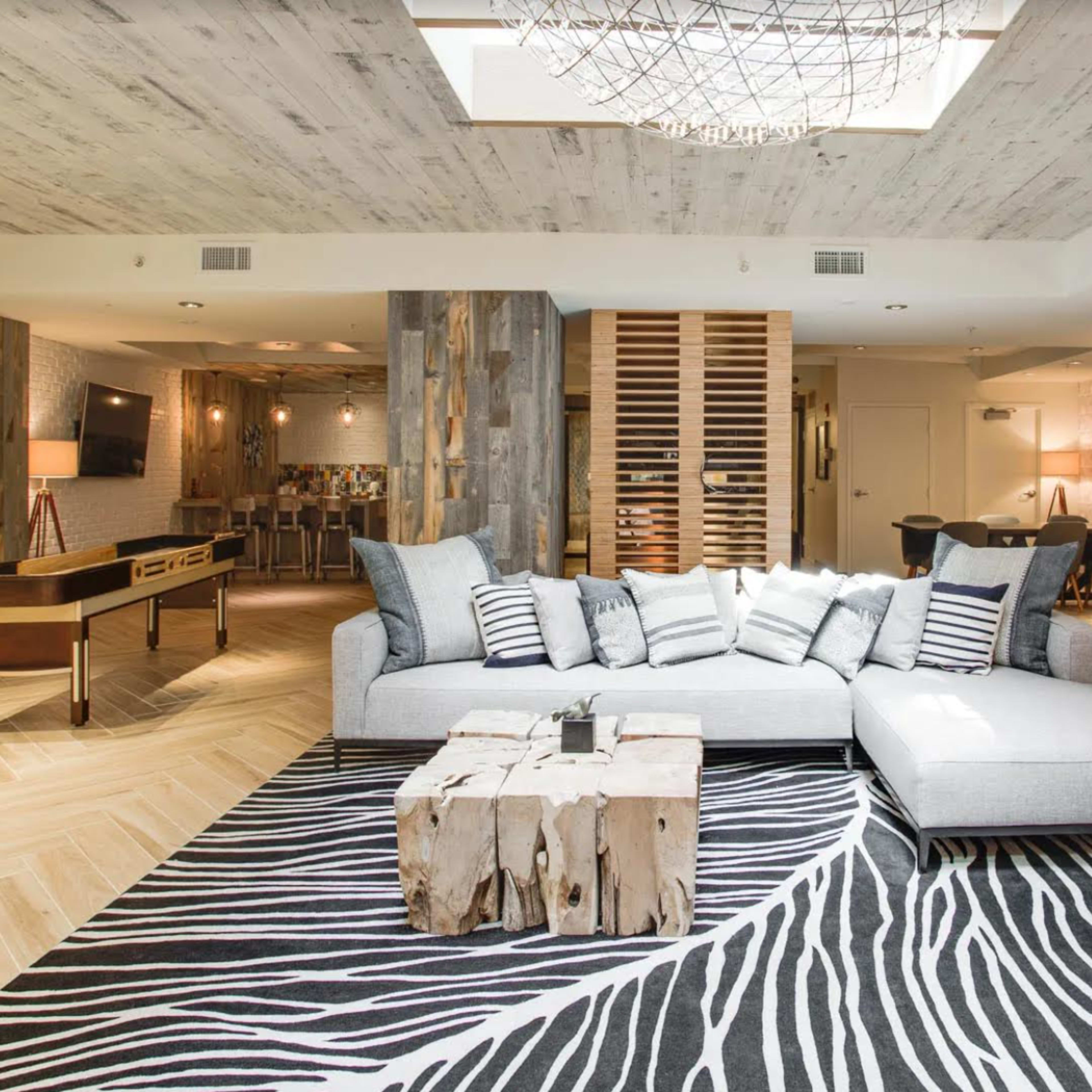 A spacious, modern living area featuring a light gray sectional sofa, a rustic wooden coffee table, and a striped black-and-white area rug.