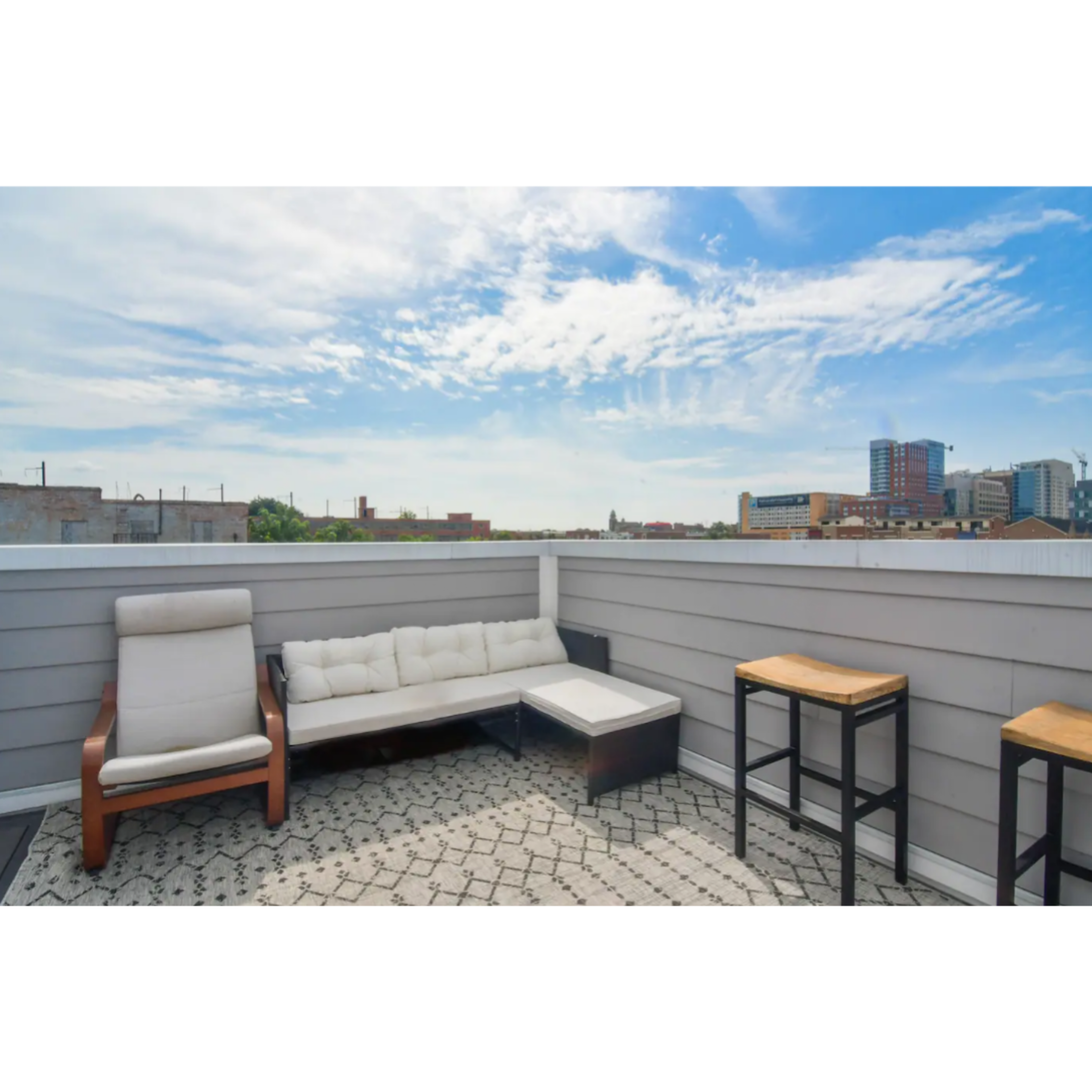 A rooftop terrace with modern outdoor furniture and a view of a city skyline under a cloudy sky.