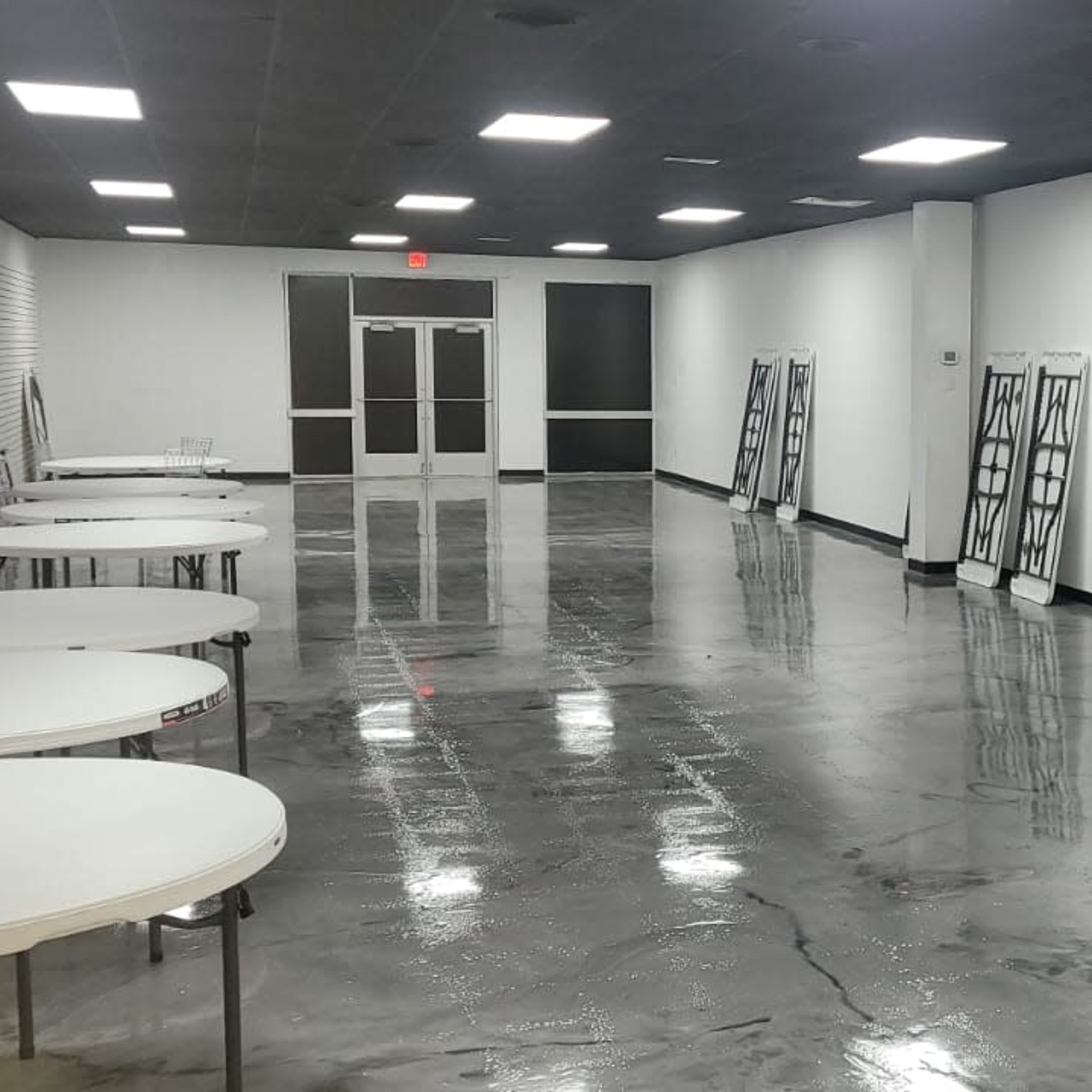 A large, empty room with several round tables lined up against the walls and a polished concrete floor.