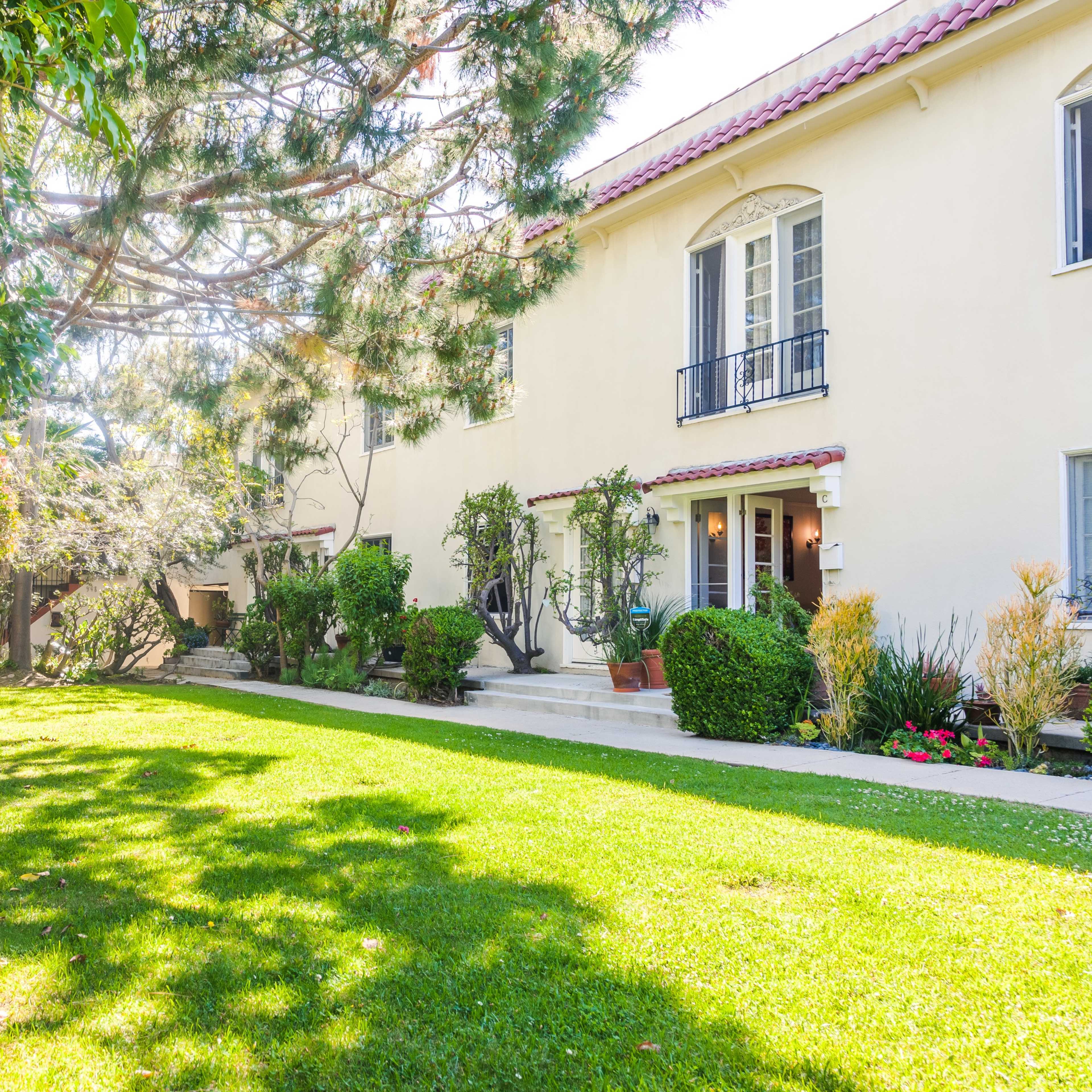 A well-maintained two-story building is set in a lush green garden with various shrubs and trees.