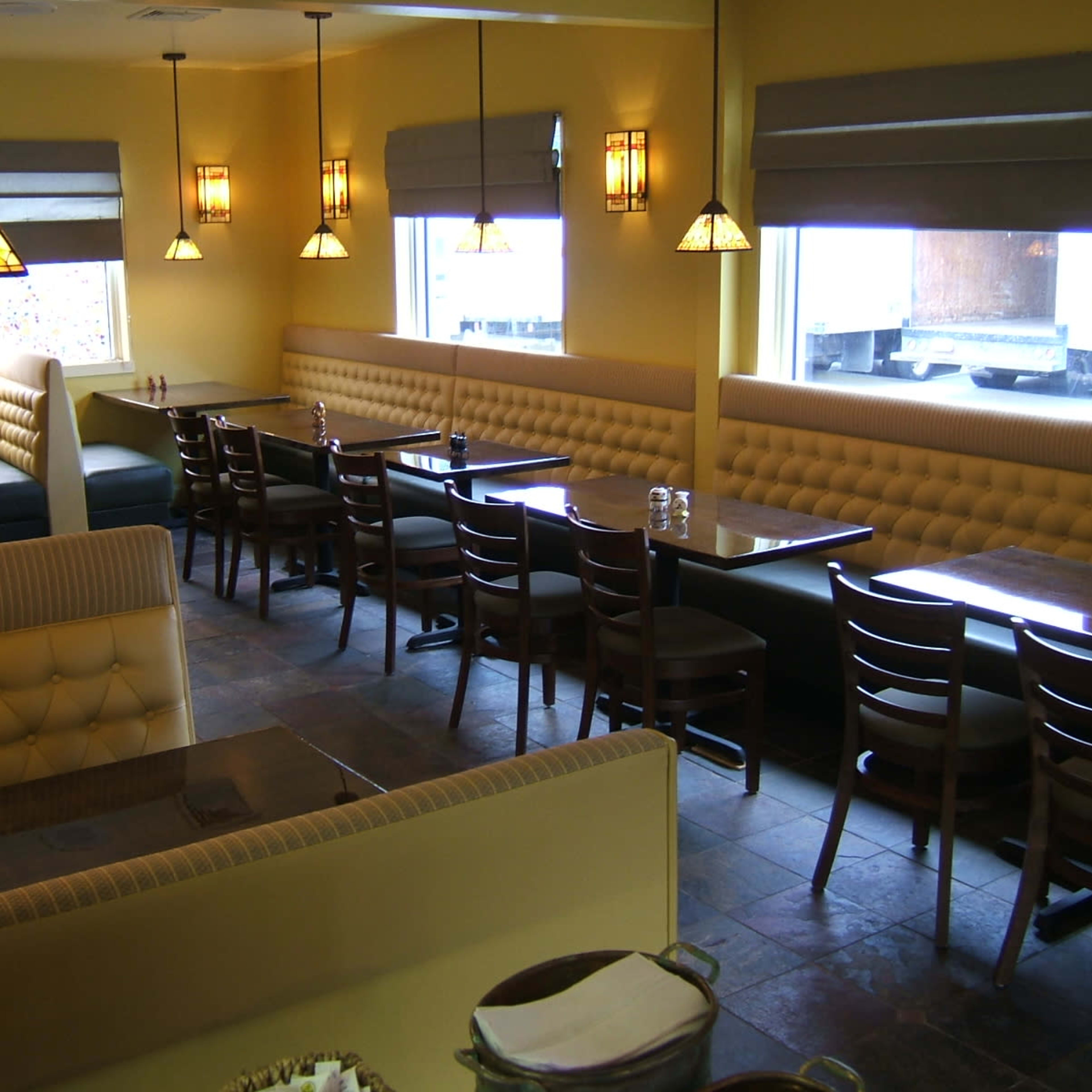 A restaurant interior featuring yellow walls, booth seating, and wooden tables arranged under pendant lighting.