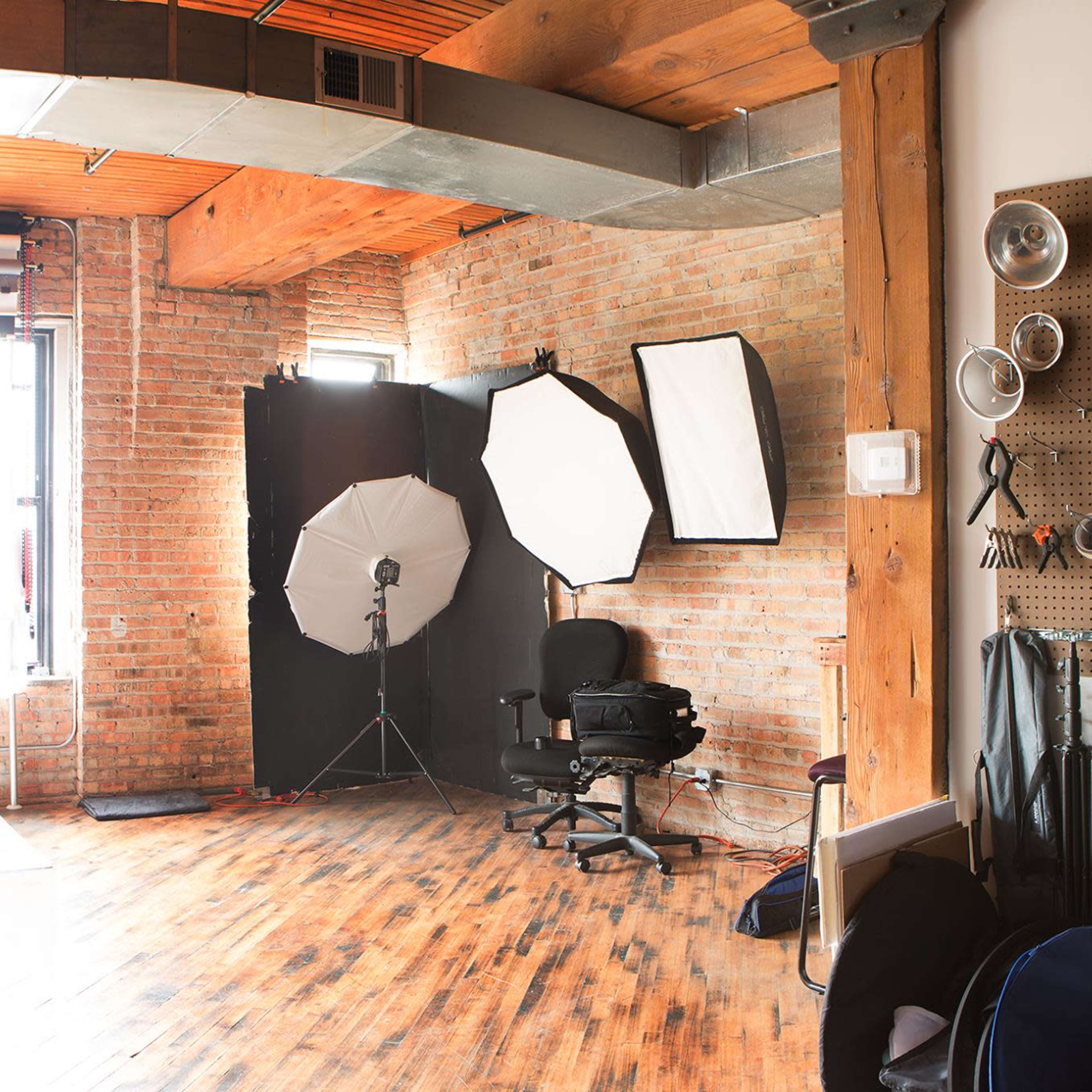 A photography studio with various lighting equipment, a backdrop, and large windows letting in natural light.