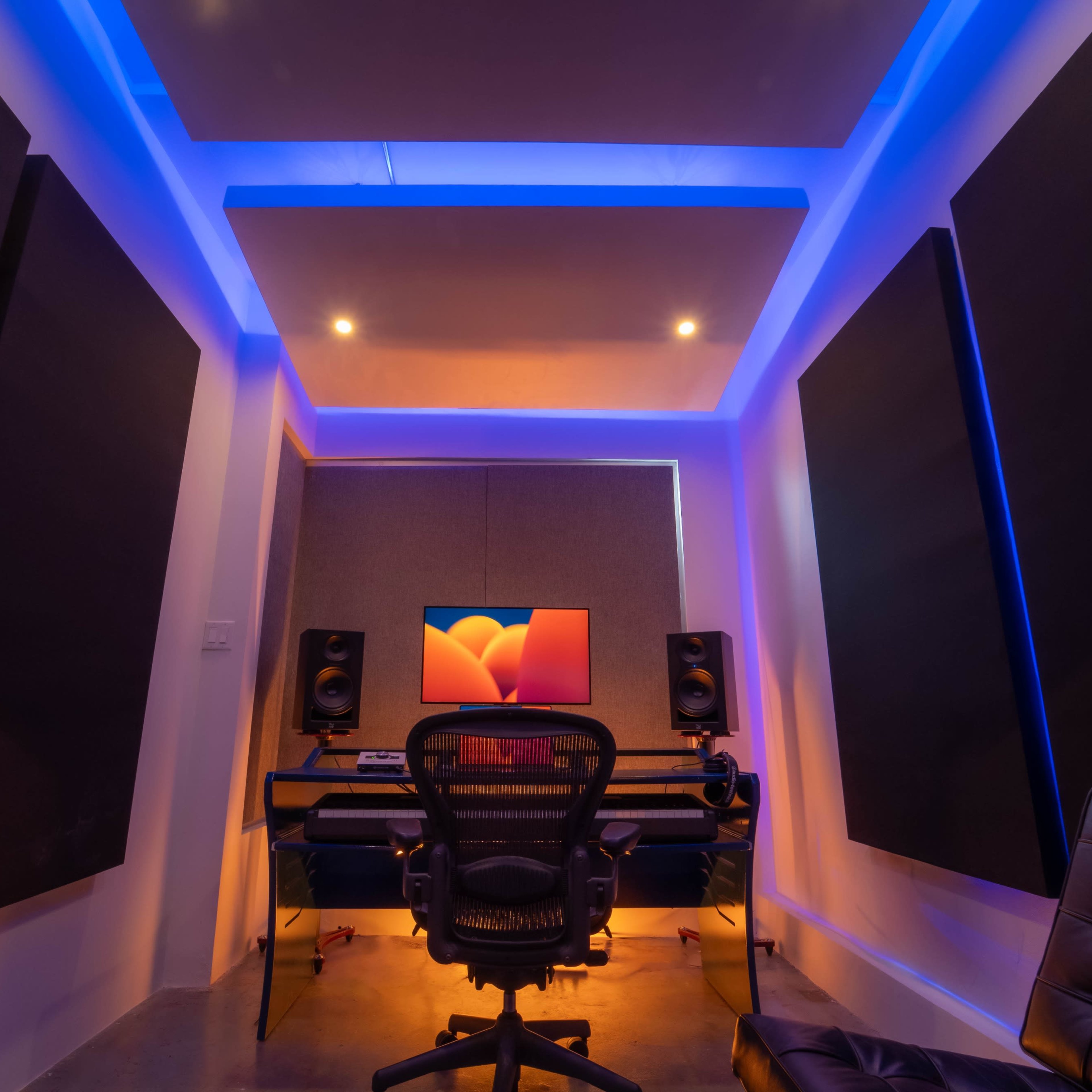 A modern audio recording studio featuring a computer desk, a chair, and soundproofing panels on the walls.