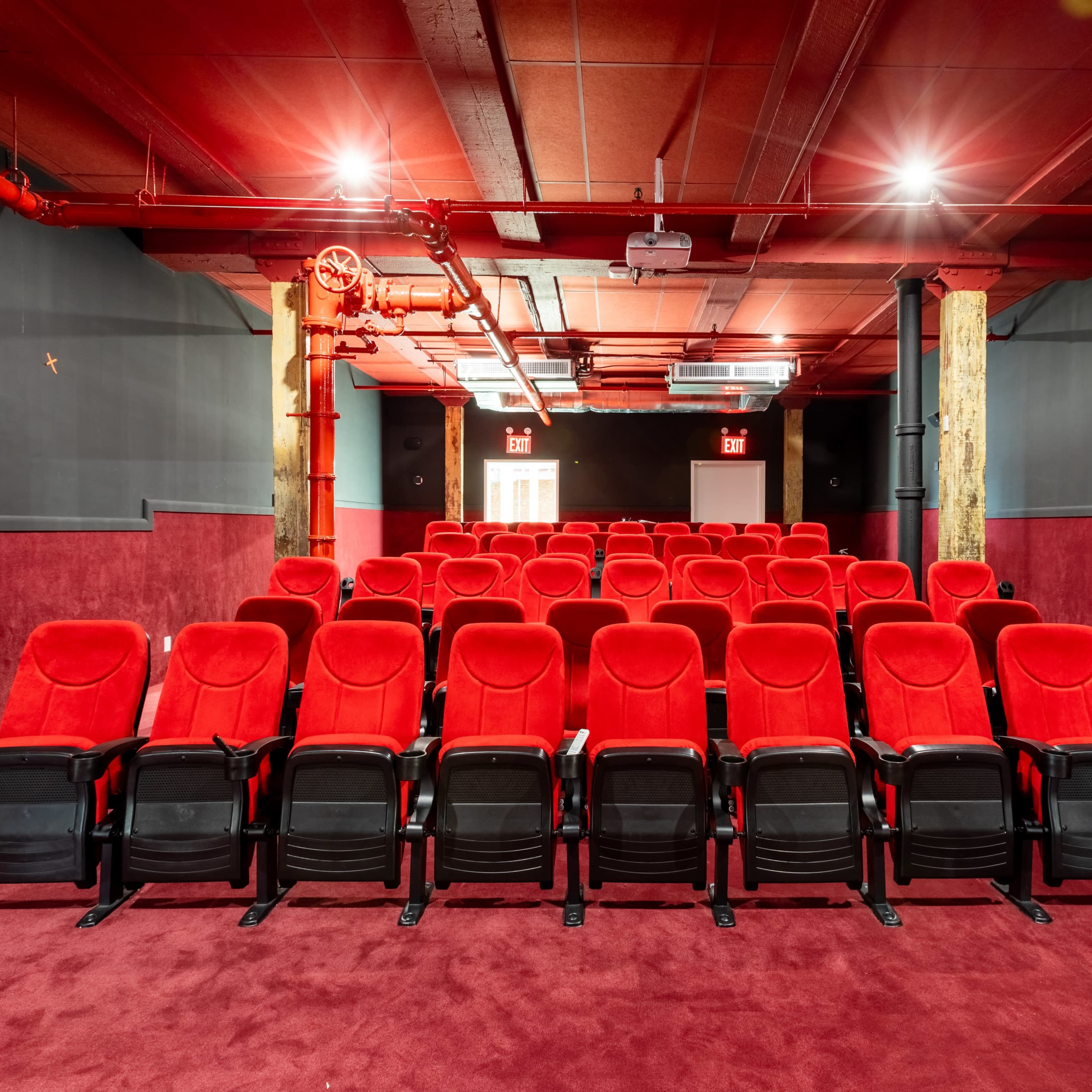 A small, modern theater with rows of red seats set against dark walls and a carpeted floor.