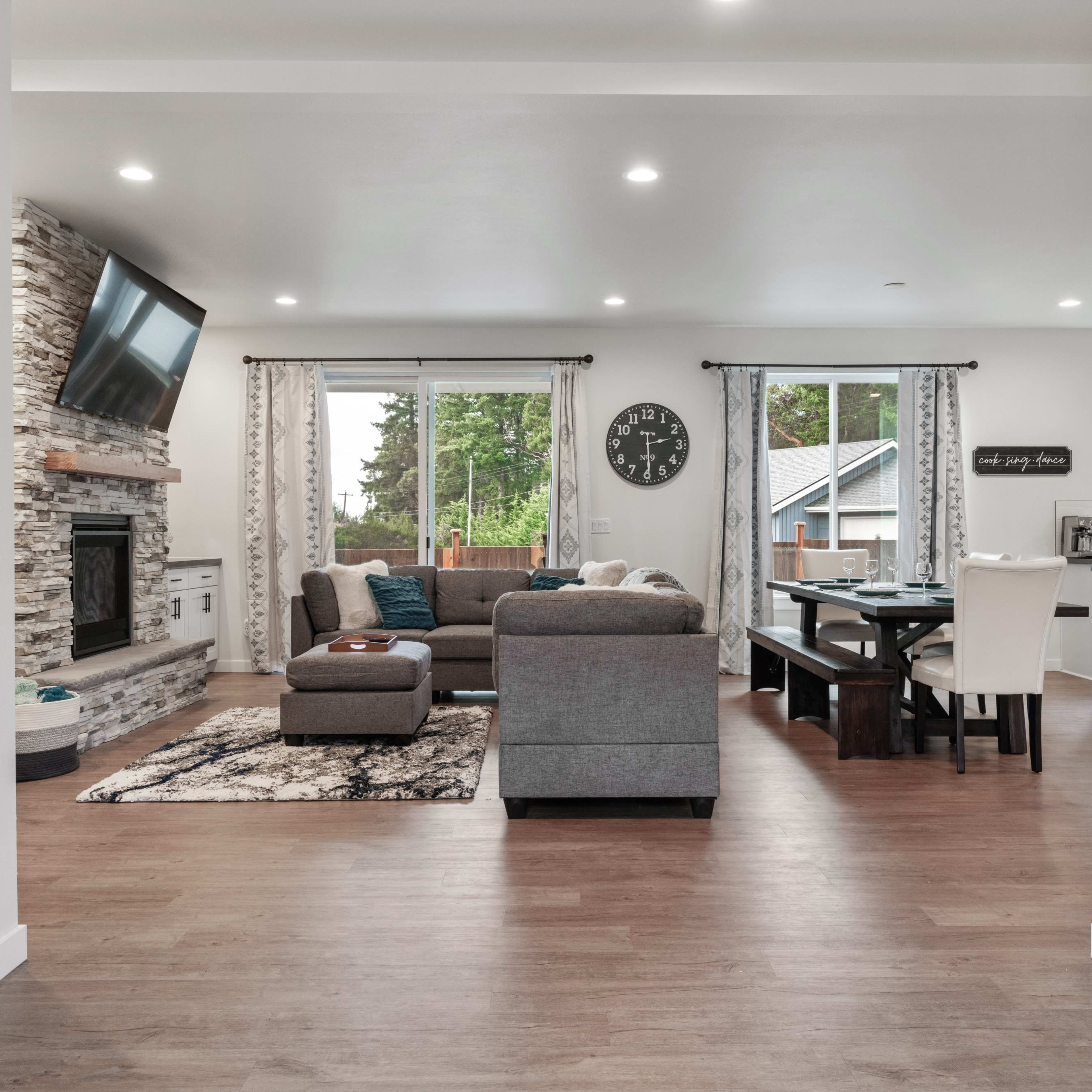 A modern living space with a gray sectional sofa, a television mounted on the wall, and a dining area with a table and chairs.
