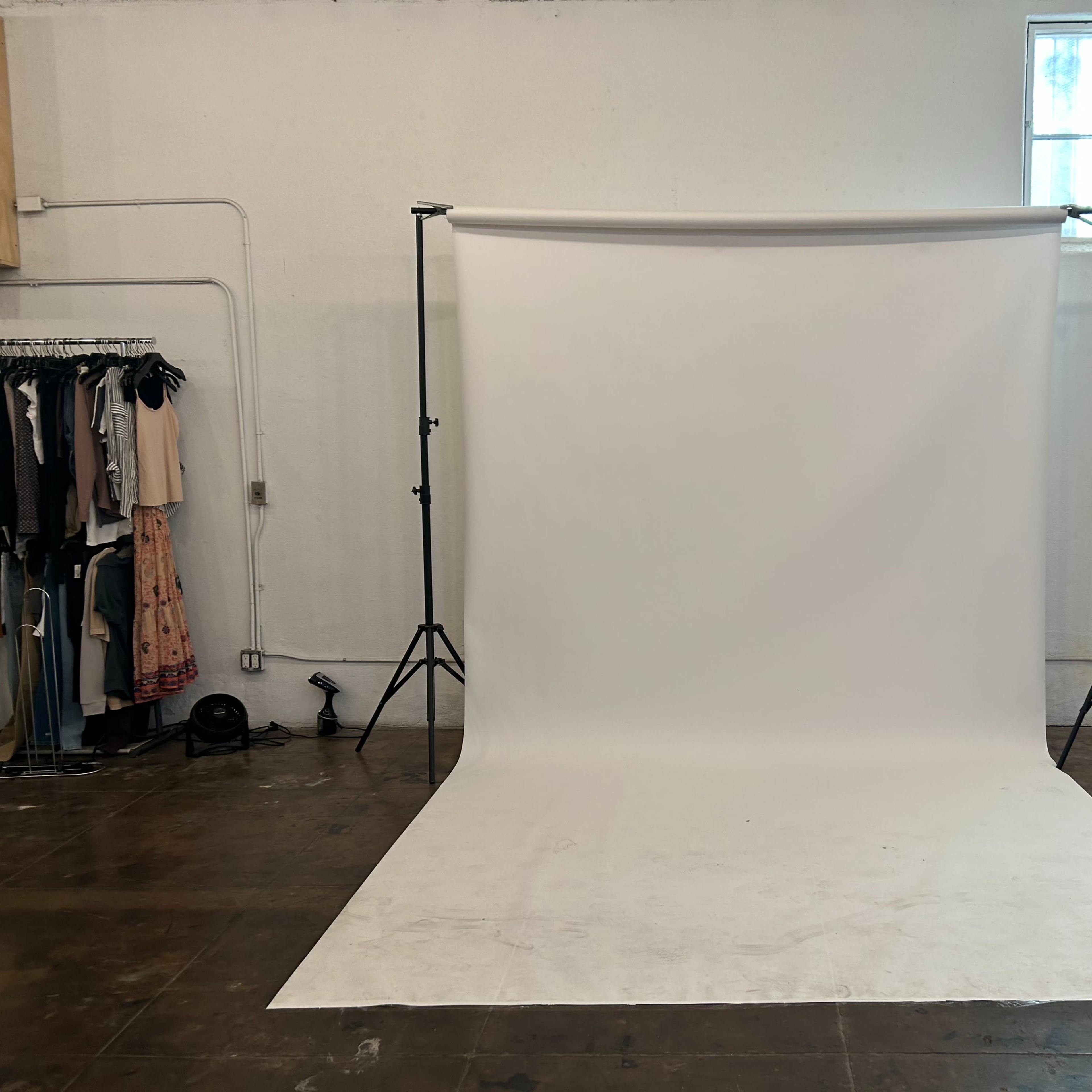 An empty photography studio with a white backdrop supported by two black stands.