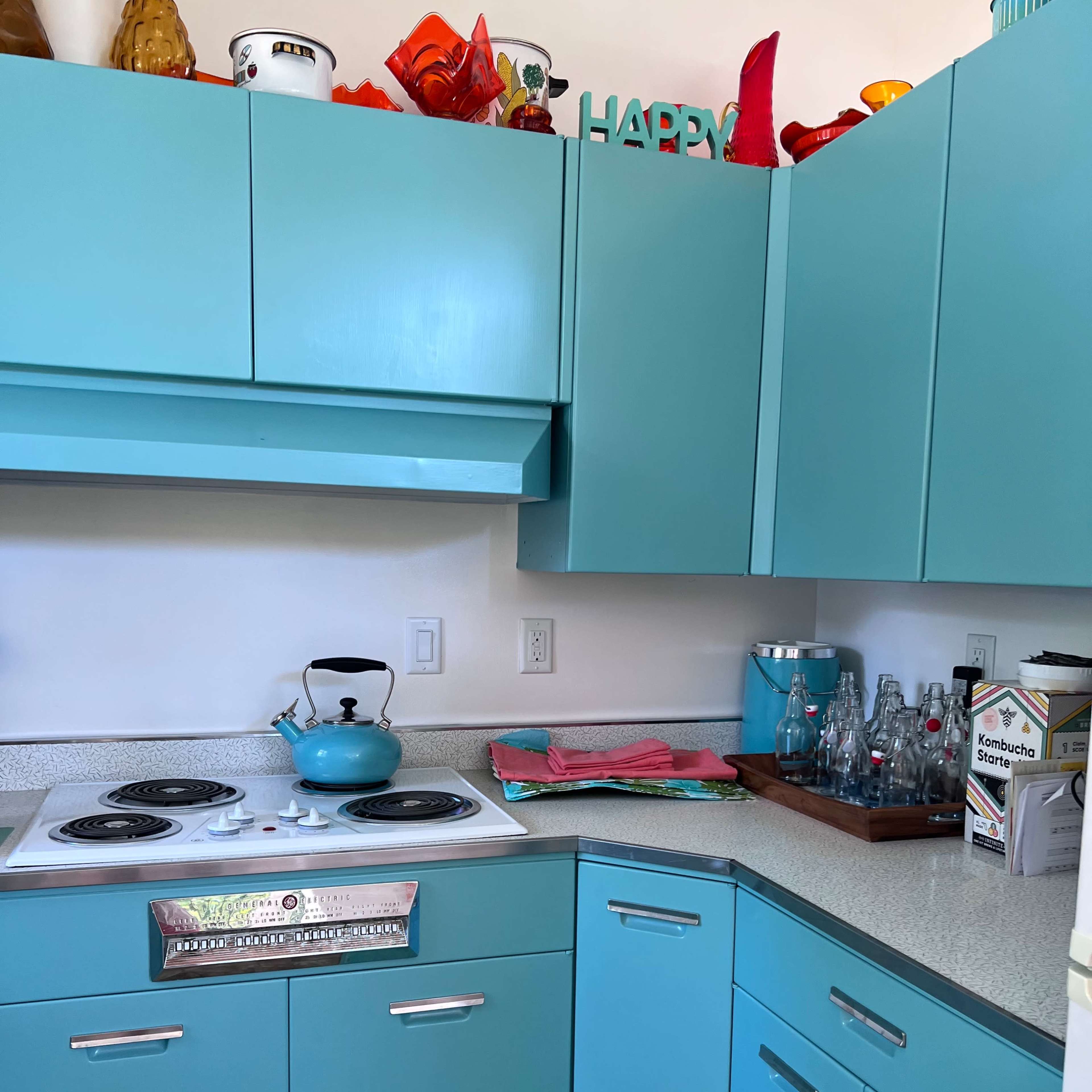 A small kitchen with turquoise cabinets, a vintage stove, and colorful decor on the shelves.