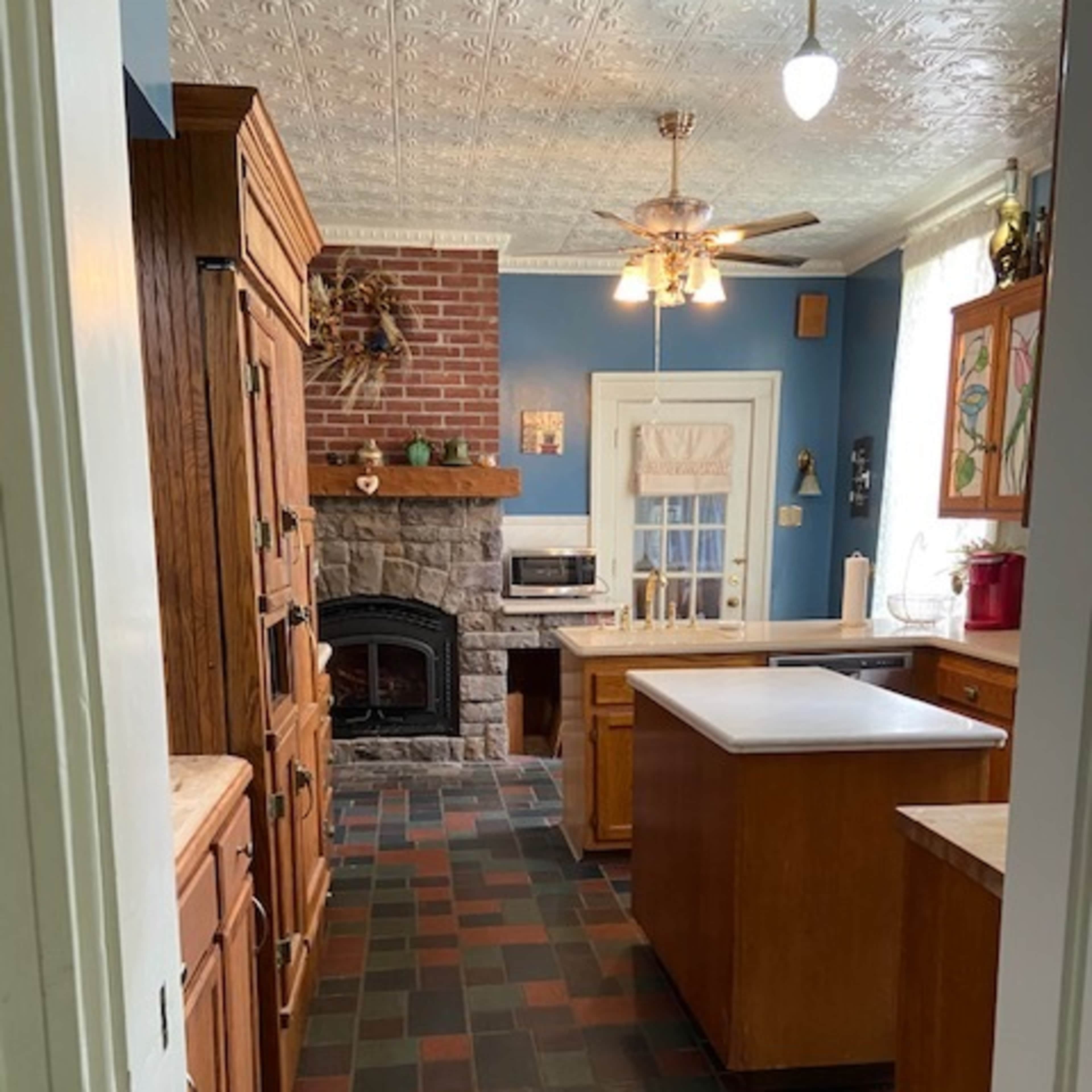 A kitchen with wooden cabinets, a stone fireplace, and a central island, featuring a tiled floor in dark and light colors.