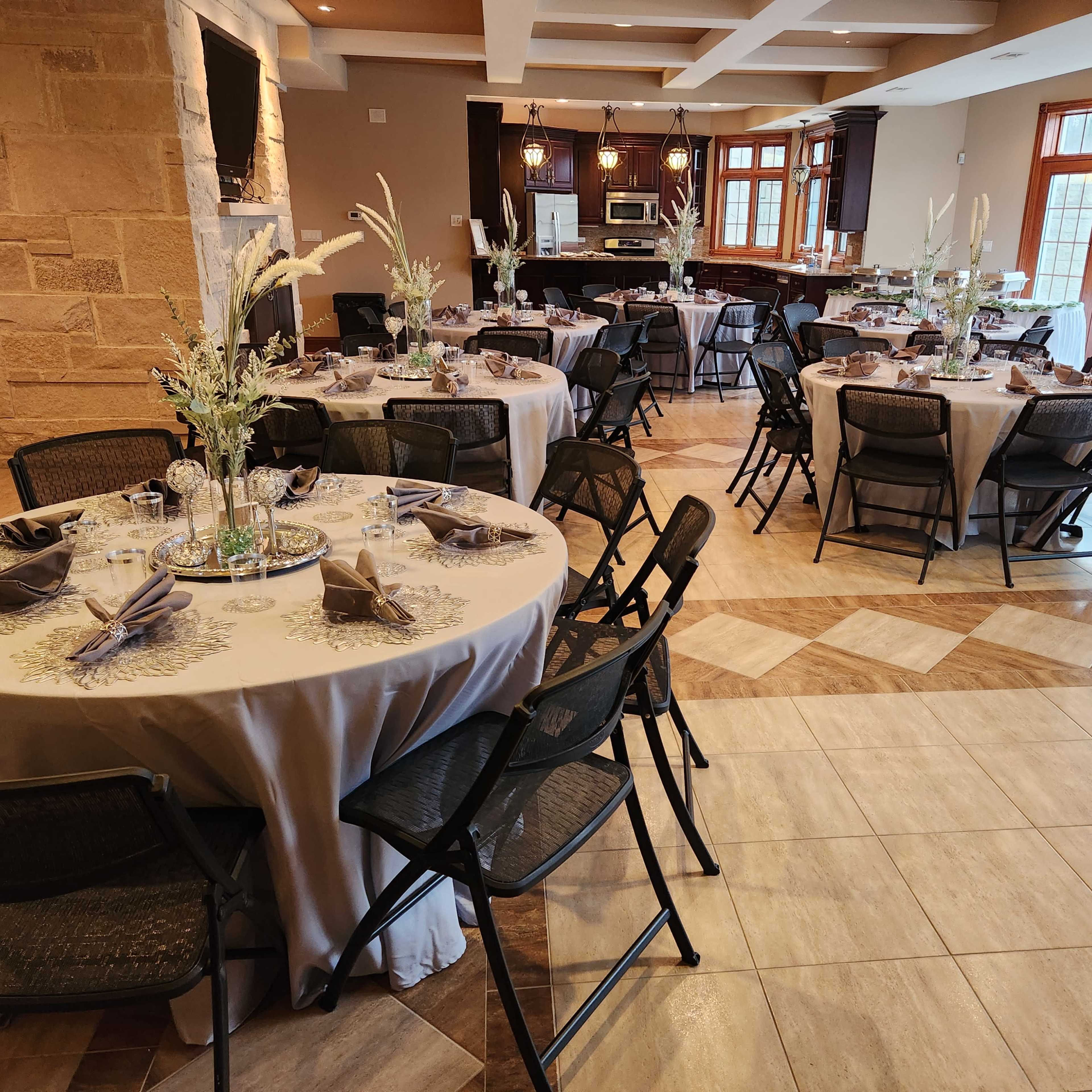 A neatly arranged dining area with several round tables covered in tablecloths, each set with dishes and centerpieces, surrounded by black folding chairs.