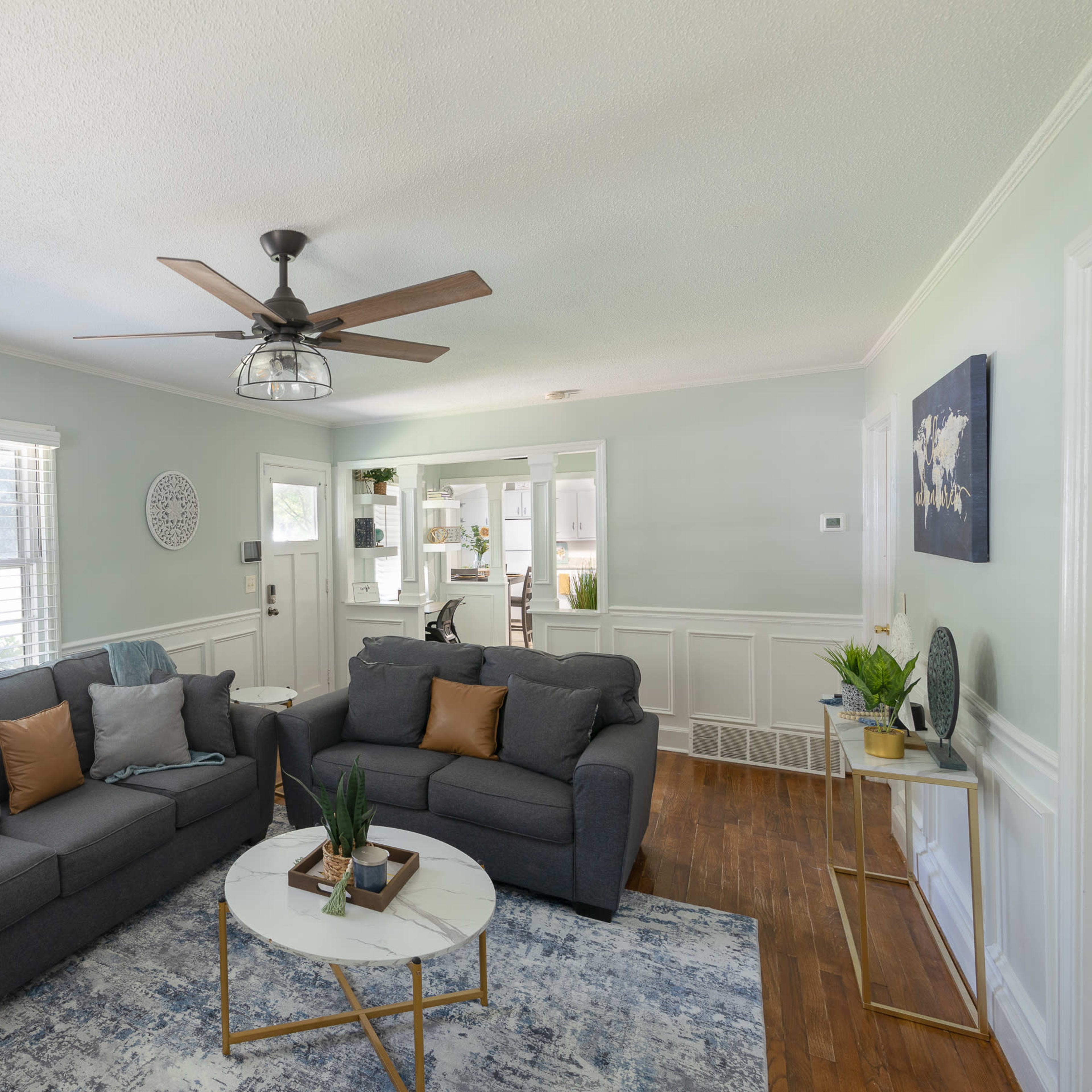 A living room with two gray sofas, a round coffee table, and a ceiling fan, all set against light green walls and hardwood flooring.