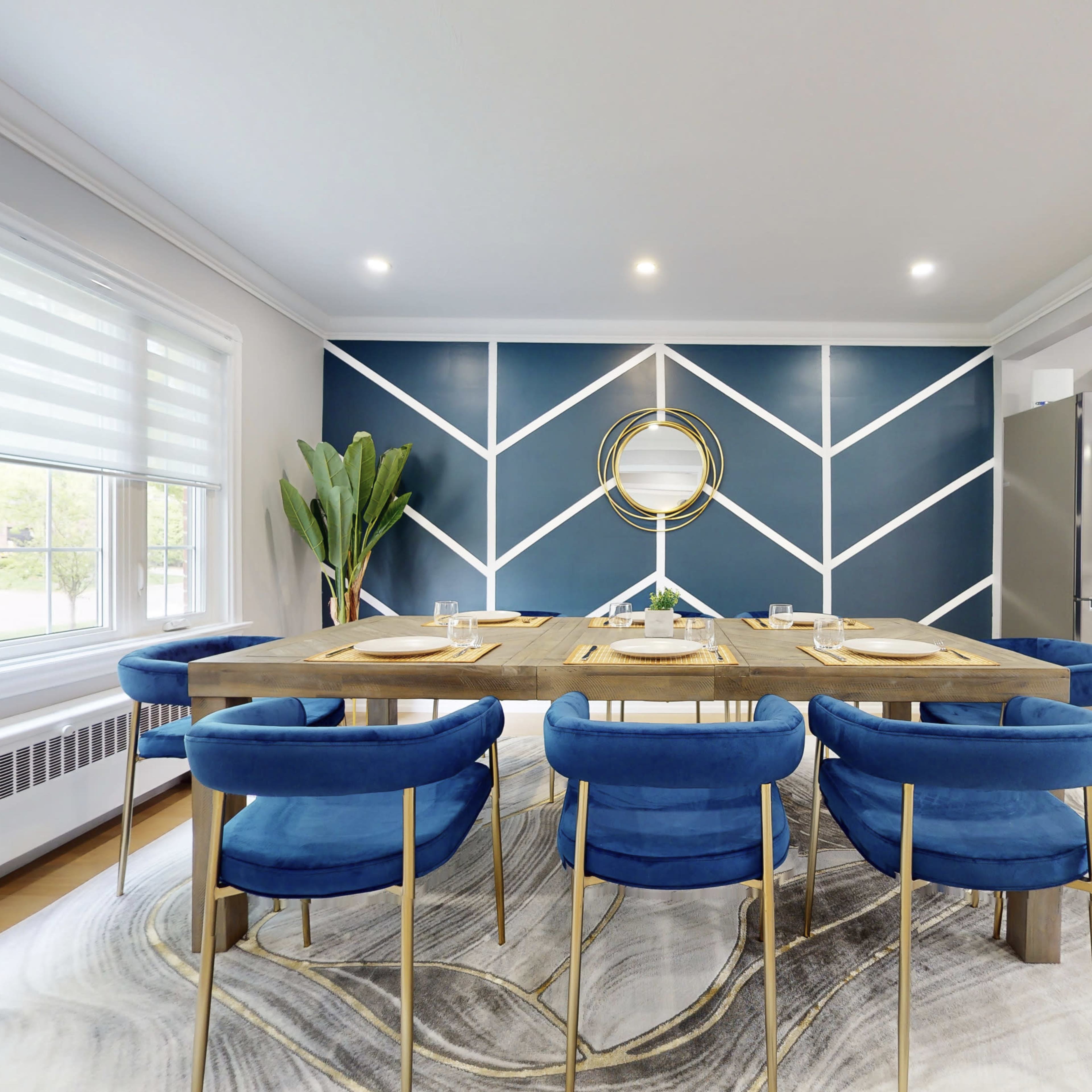 A modern dining area with a large wooden table surrounded by blue chairs, set against a blue geometric accent wall.