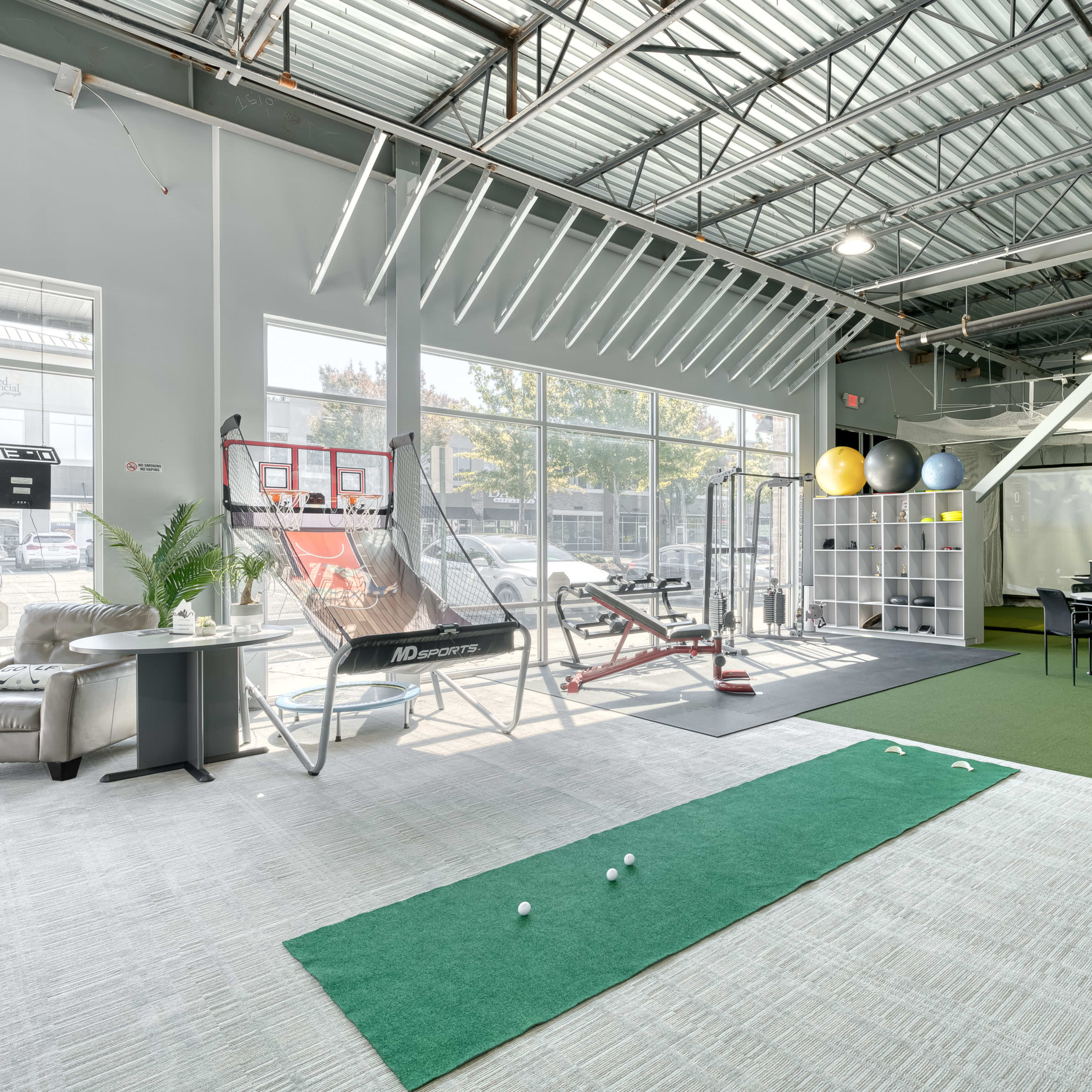 A spacious indoor training facility with a putting green, exercise equipment, and a desk area.