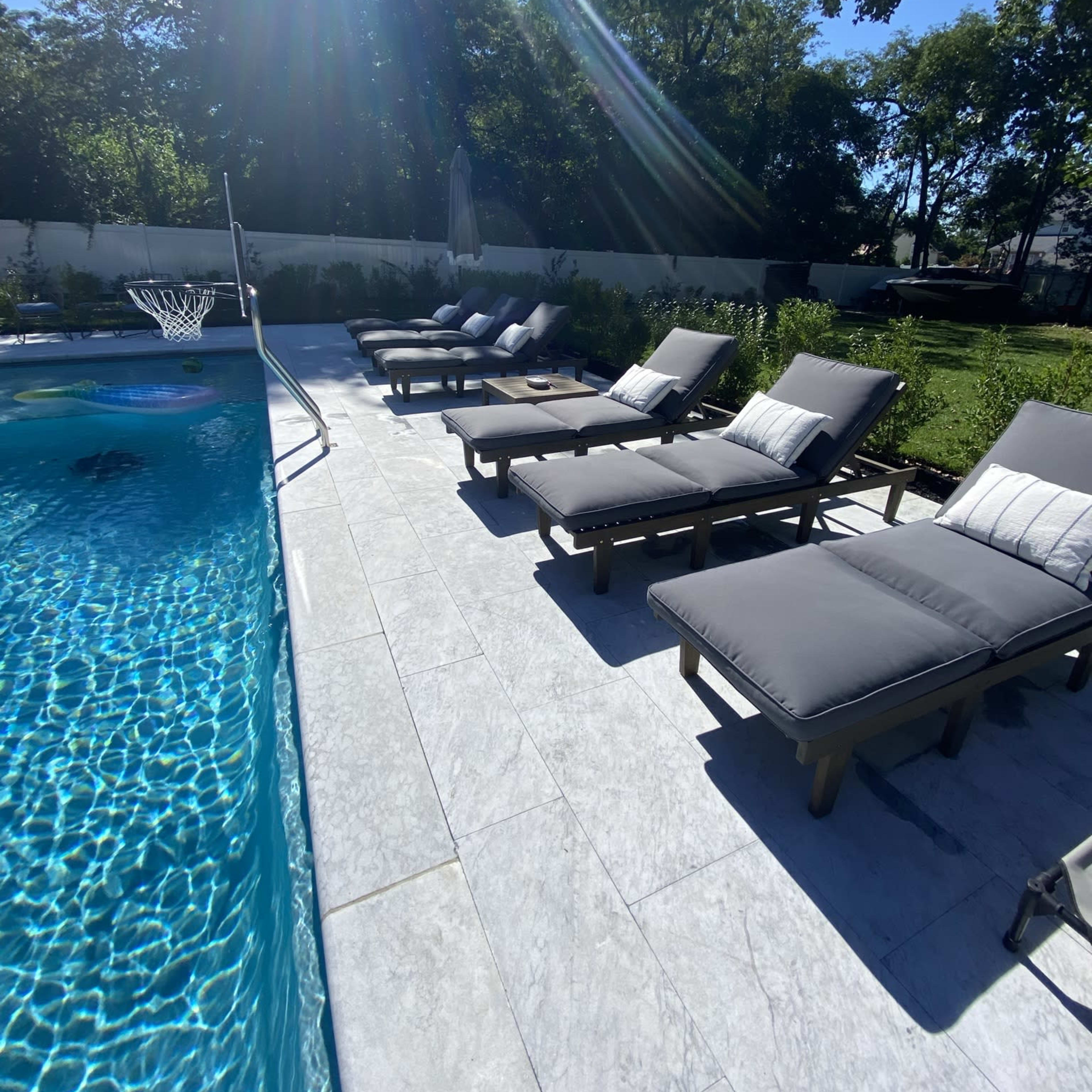 A swimming pool surrounded by several lounge chairs on a sunlit patio.