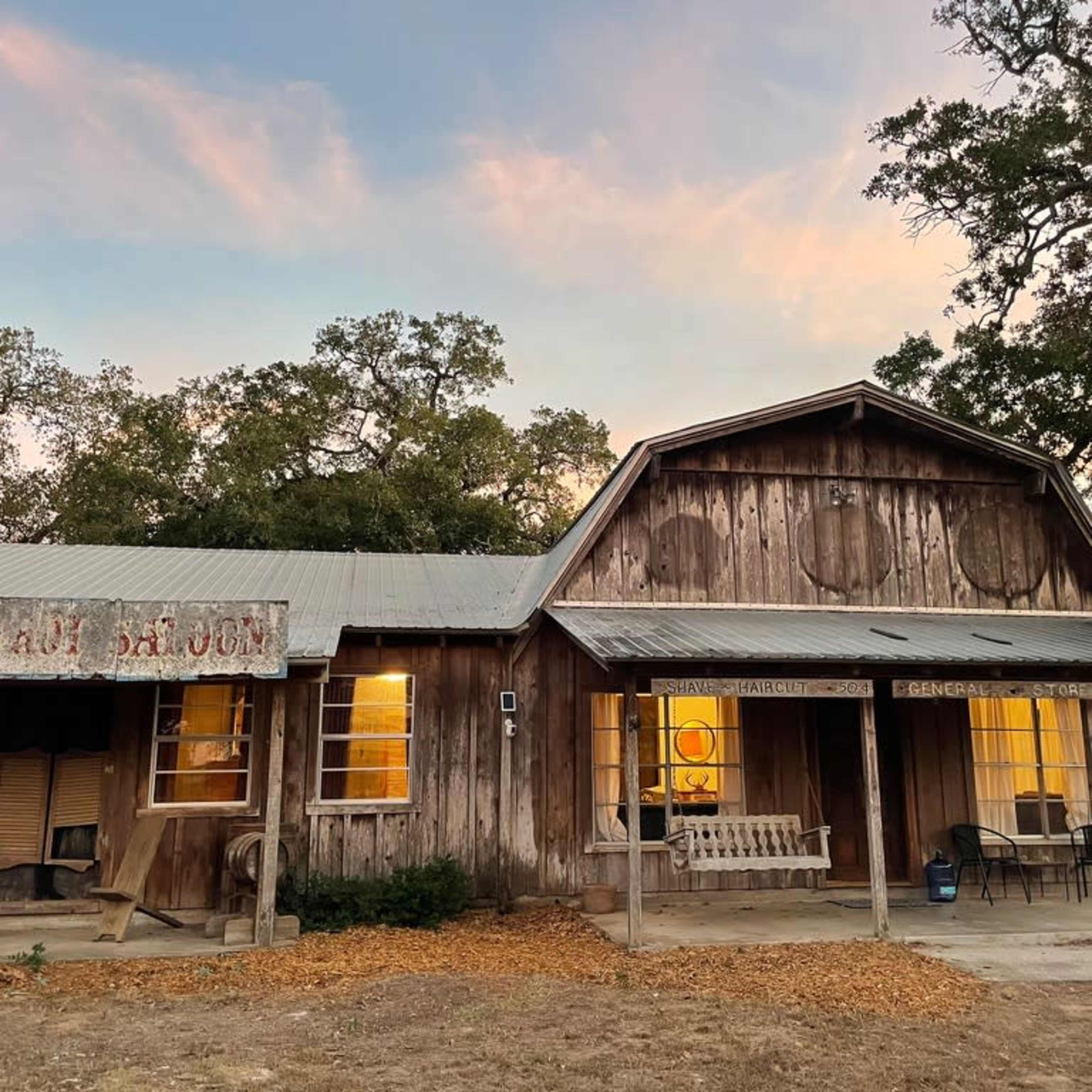 A weathered wooden building with a porch and large windows, set against a colorful sky at dusk.