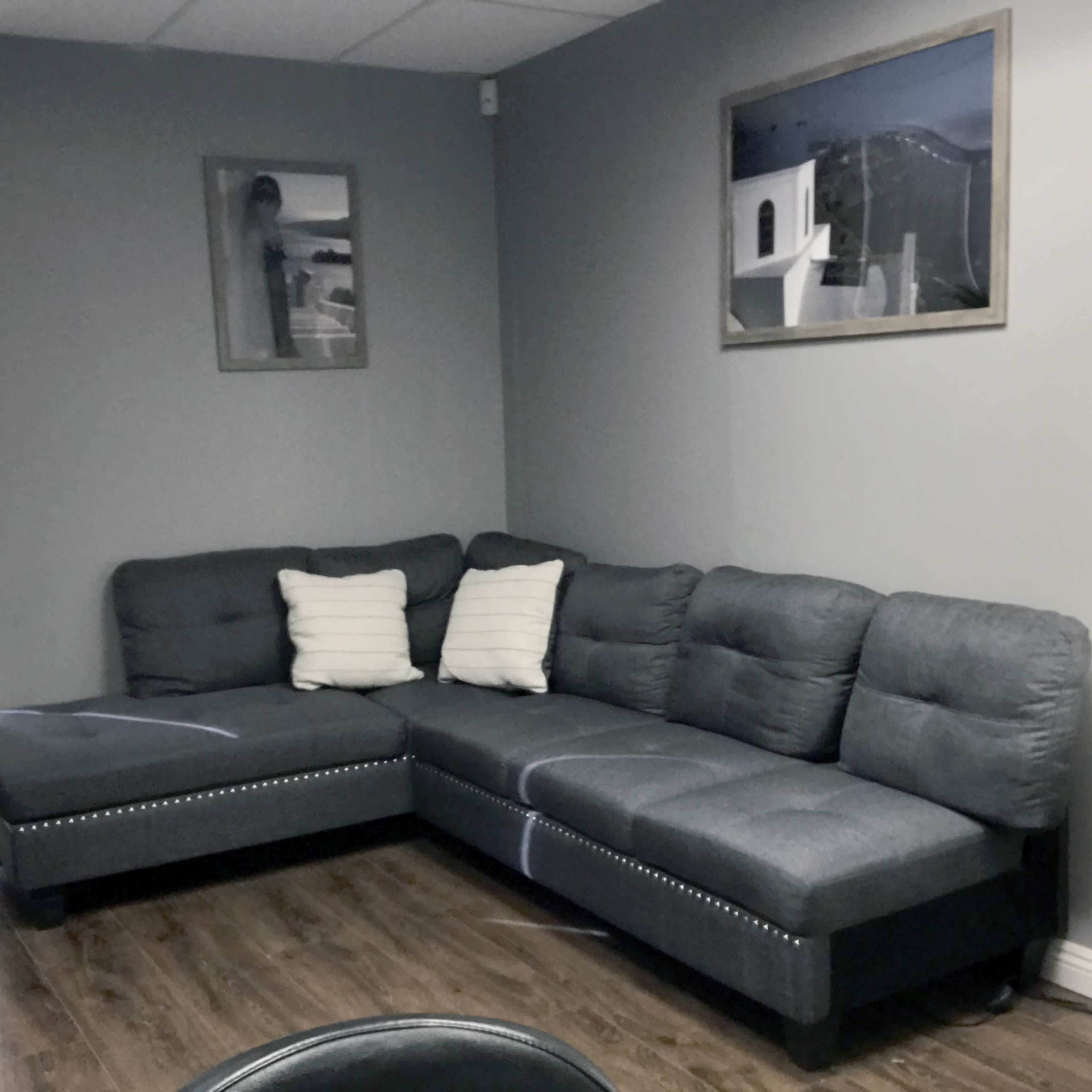 A gray sectional sofa in a well-lit corner of a room, accompanied by two white decorative pillows and a floor lamp.