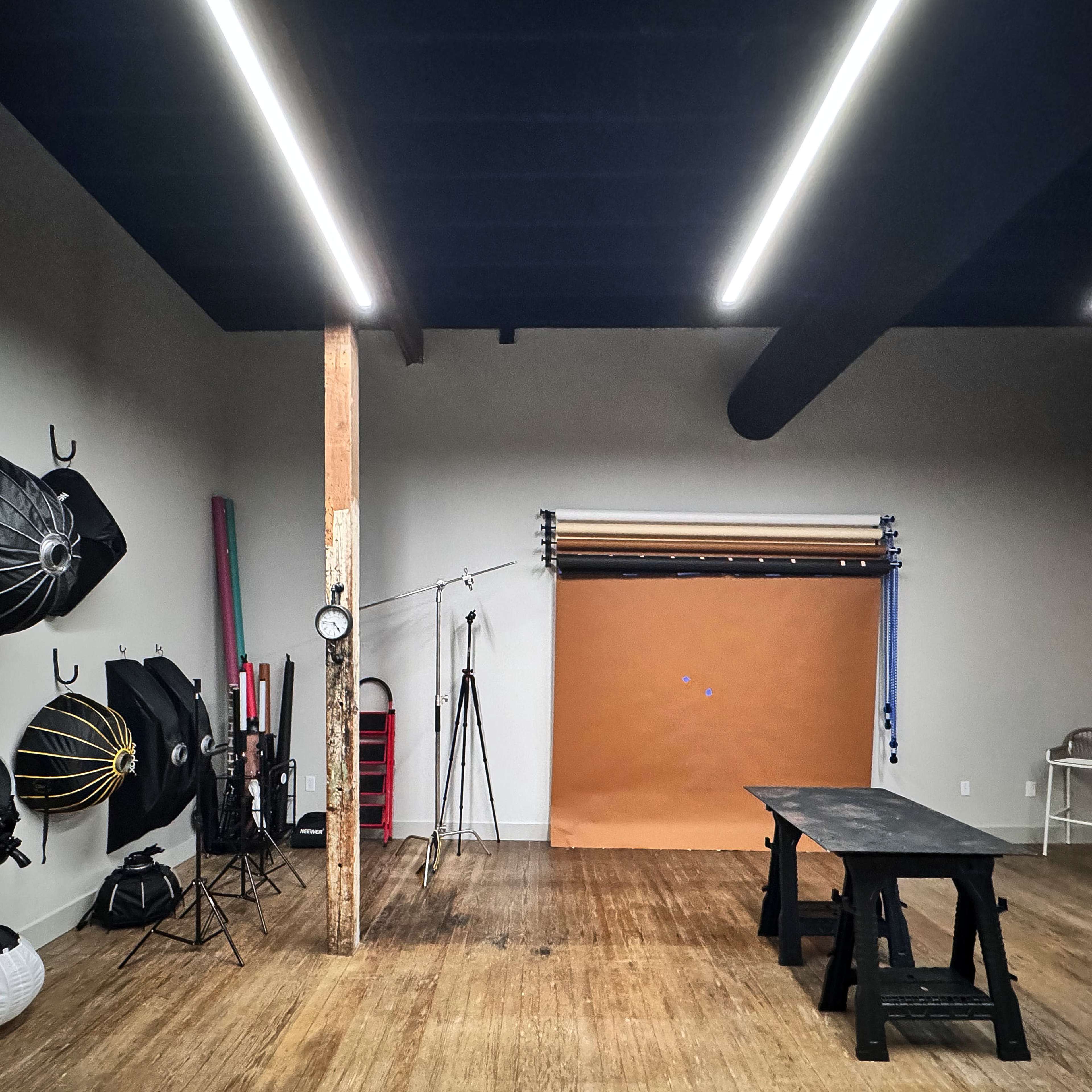 A photography studio featuring various lighting equipment, a backdrop, and wooden flooring.