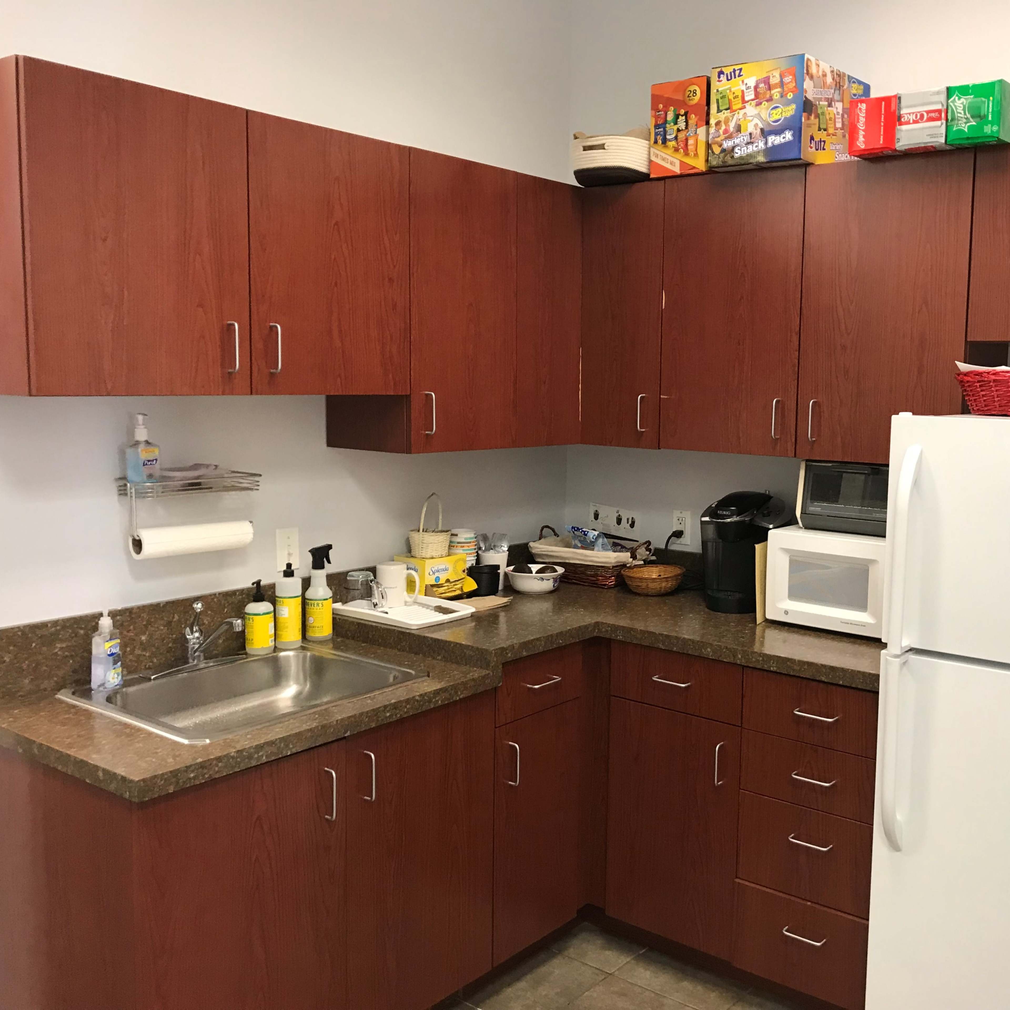 A kitchen featuring wooden cabinets, a sink, a countertop with various kitchen appliances, and a refrigerator.