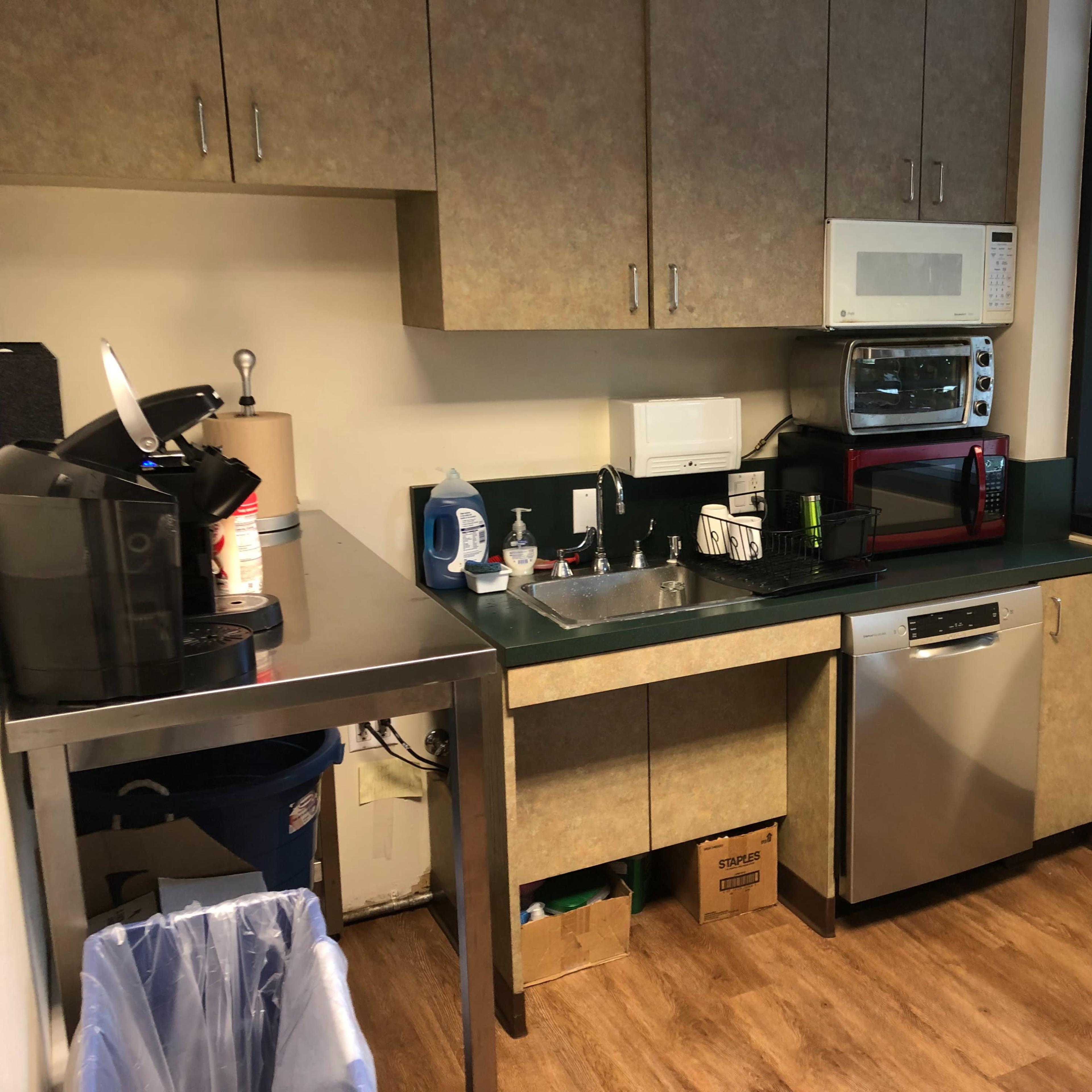 A small kitchen area with a sink, countertop appliances, and garbage bin.