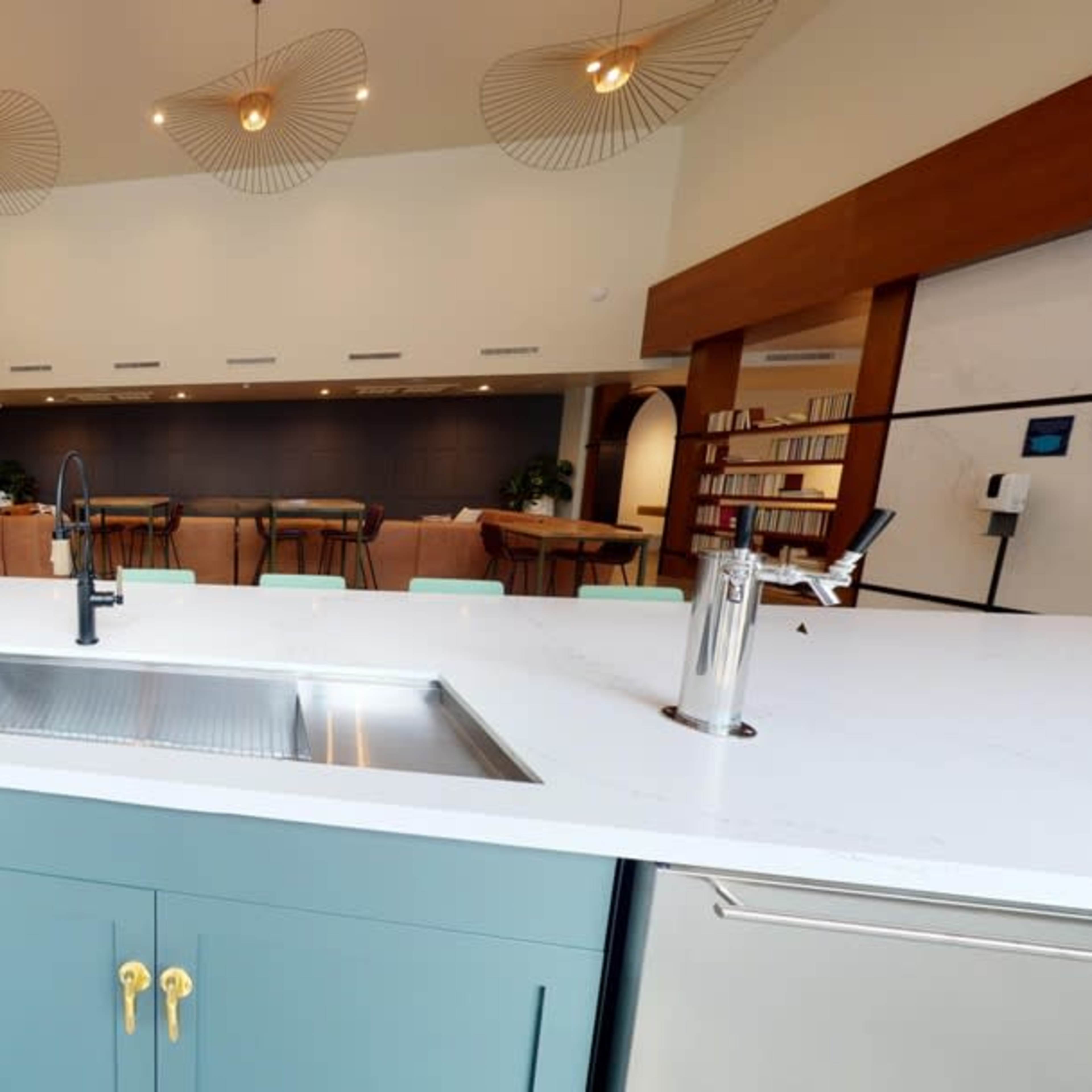 A modern kitchen featuring a large island with a stainless steel sink and cabinetry in soft blue and gray tones, illuminated by pendant lights.