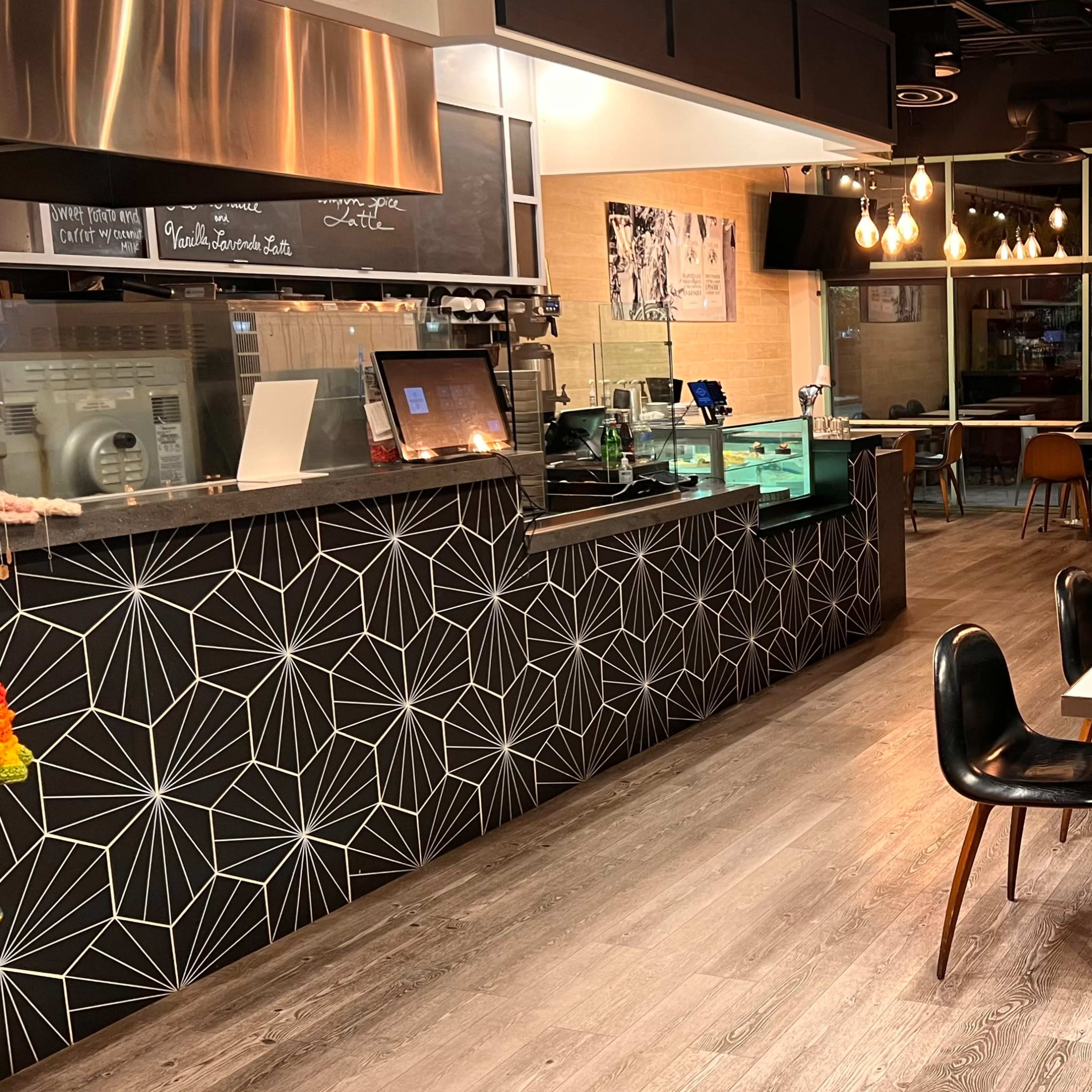 A modern café interior with a geometric patterned counter, several small tables, and a large windowed entrance.