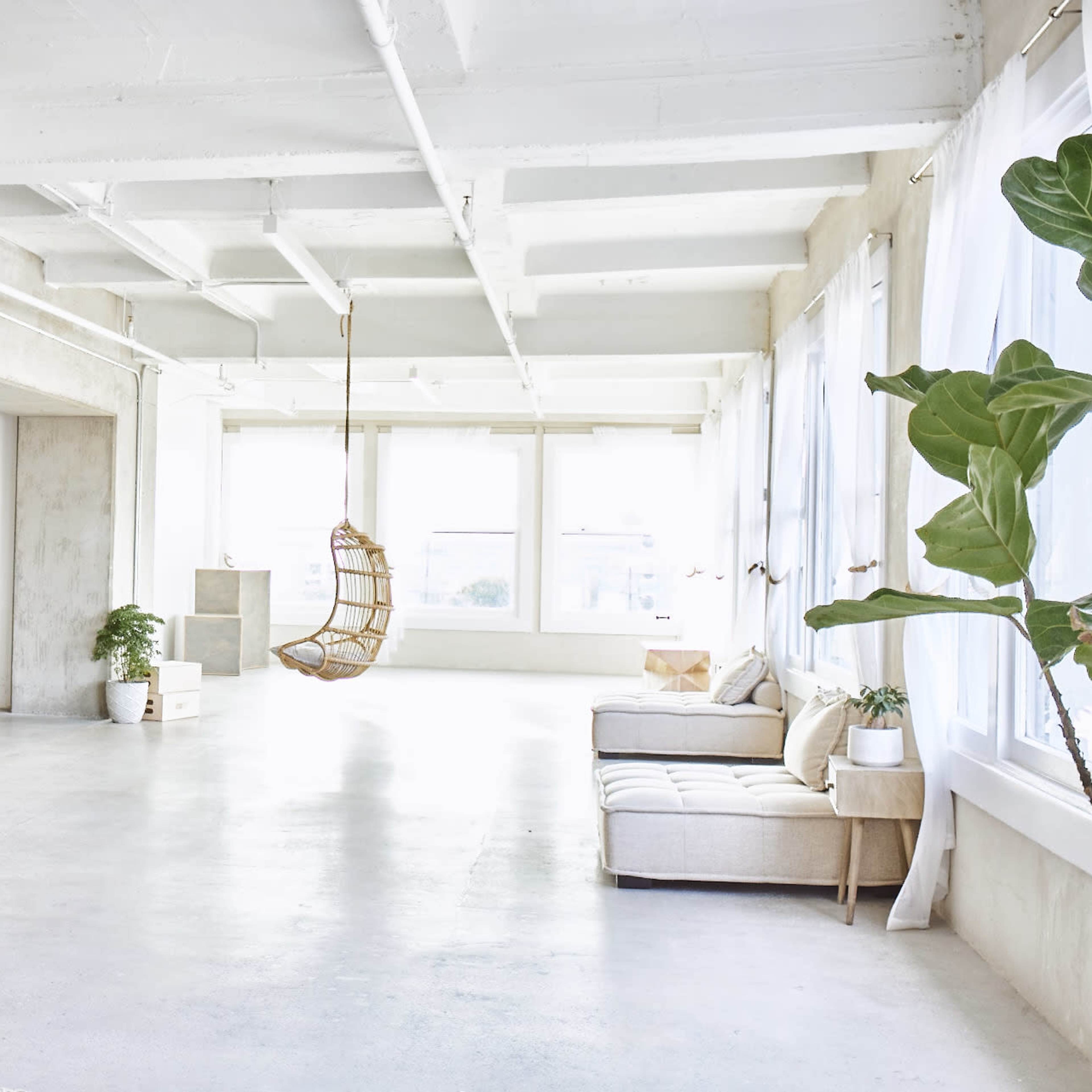 A spacious, minimalist interior features a light-colored couch, a hanging chair, and large windows that allow natural light to fill the room.