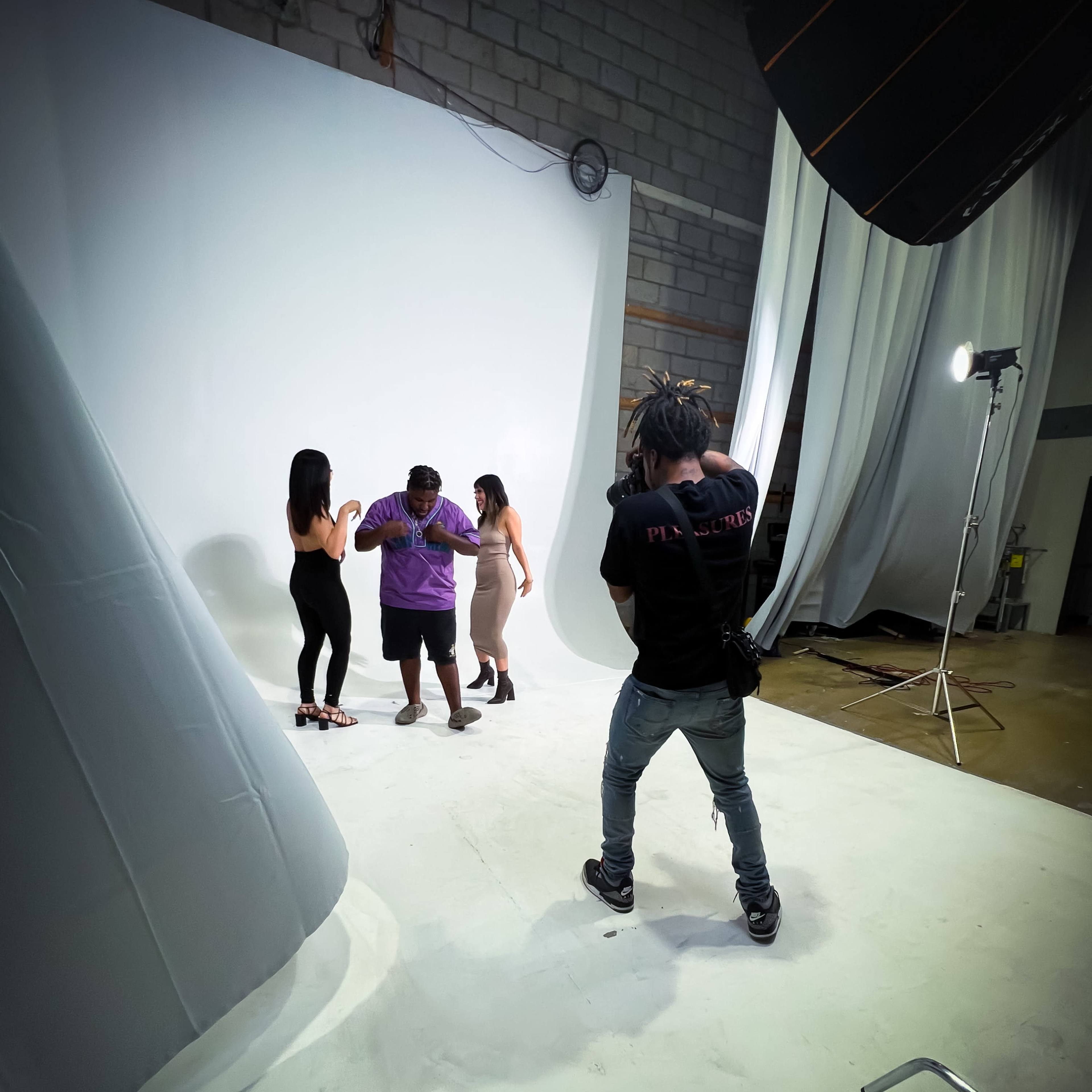 A photographer captures subjects posing in a studio with a white backdrop and soft lighting equipment.