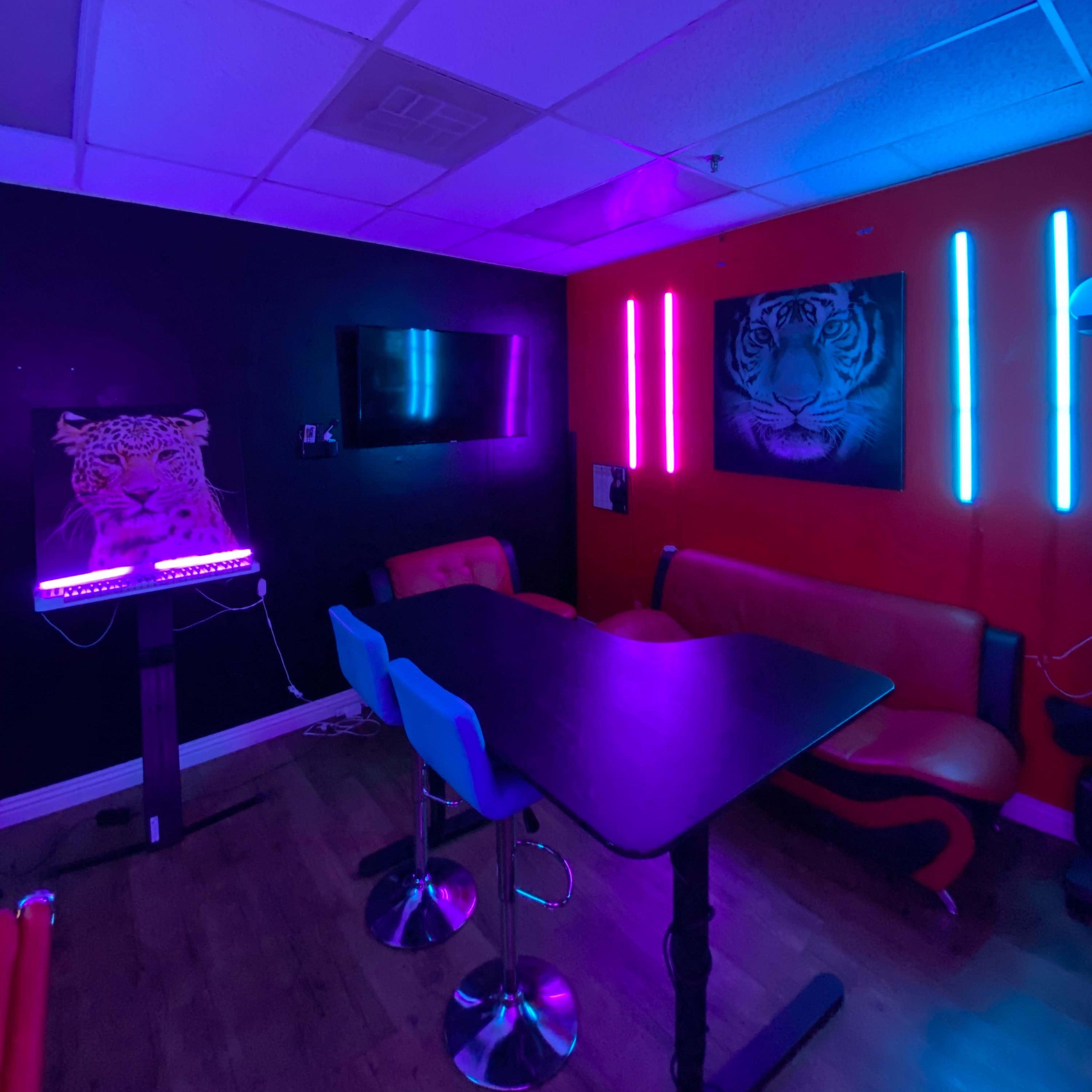 A vibrant room features a black and red color scheme, illuminated with neon lights, a table, and seating against the walls adorned with tiger-themed artwork.
