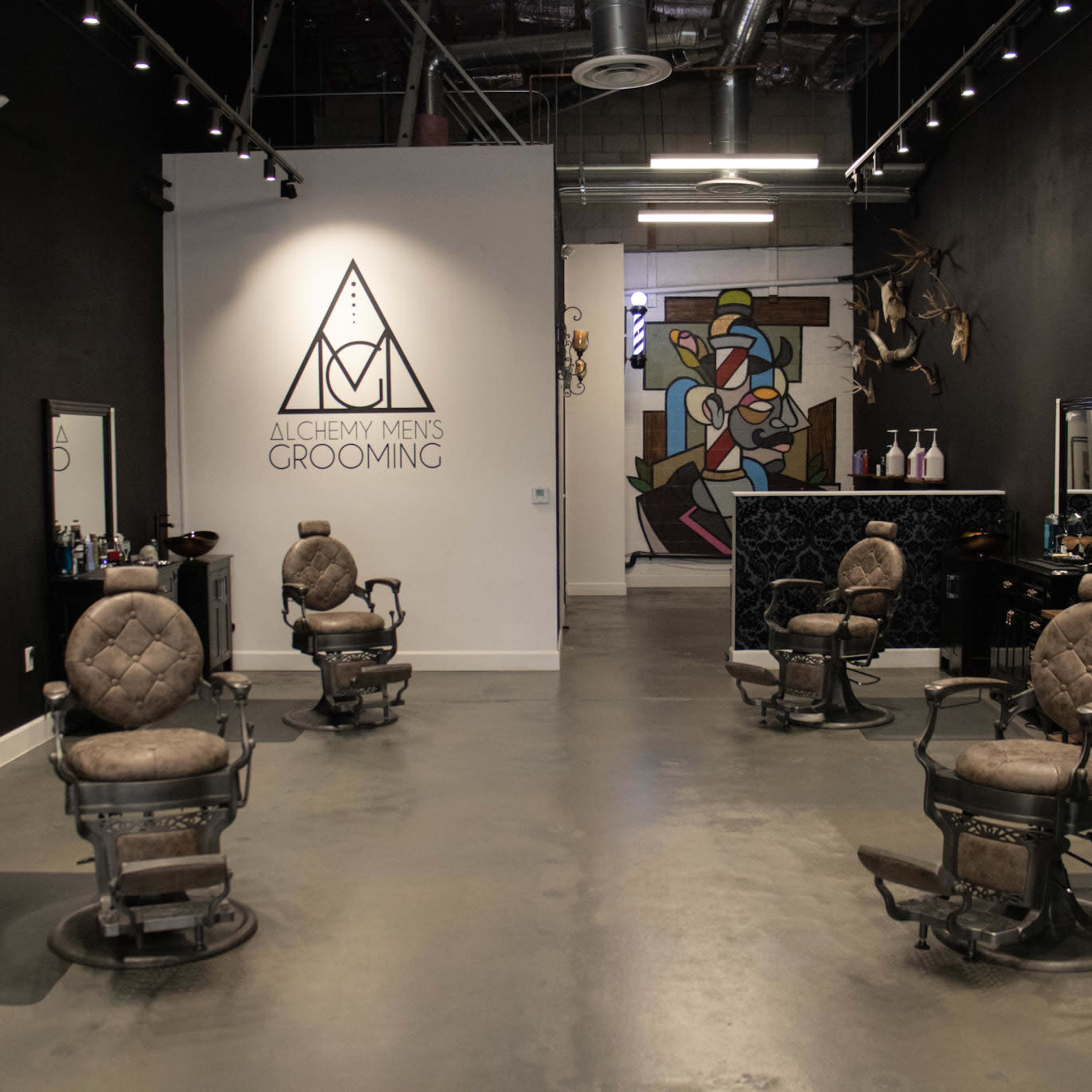 A modern barbershop with four vintage barber chairs arranged in a spacious, industrial-style interior featuring dark walls and artistic decor.