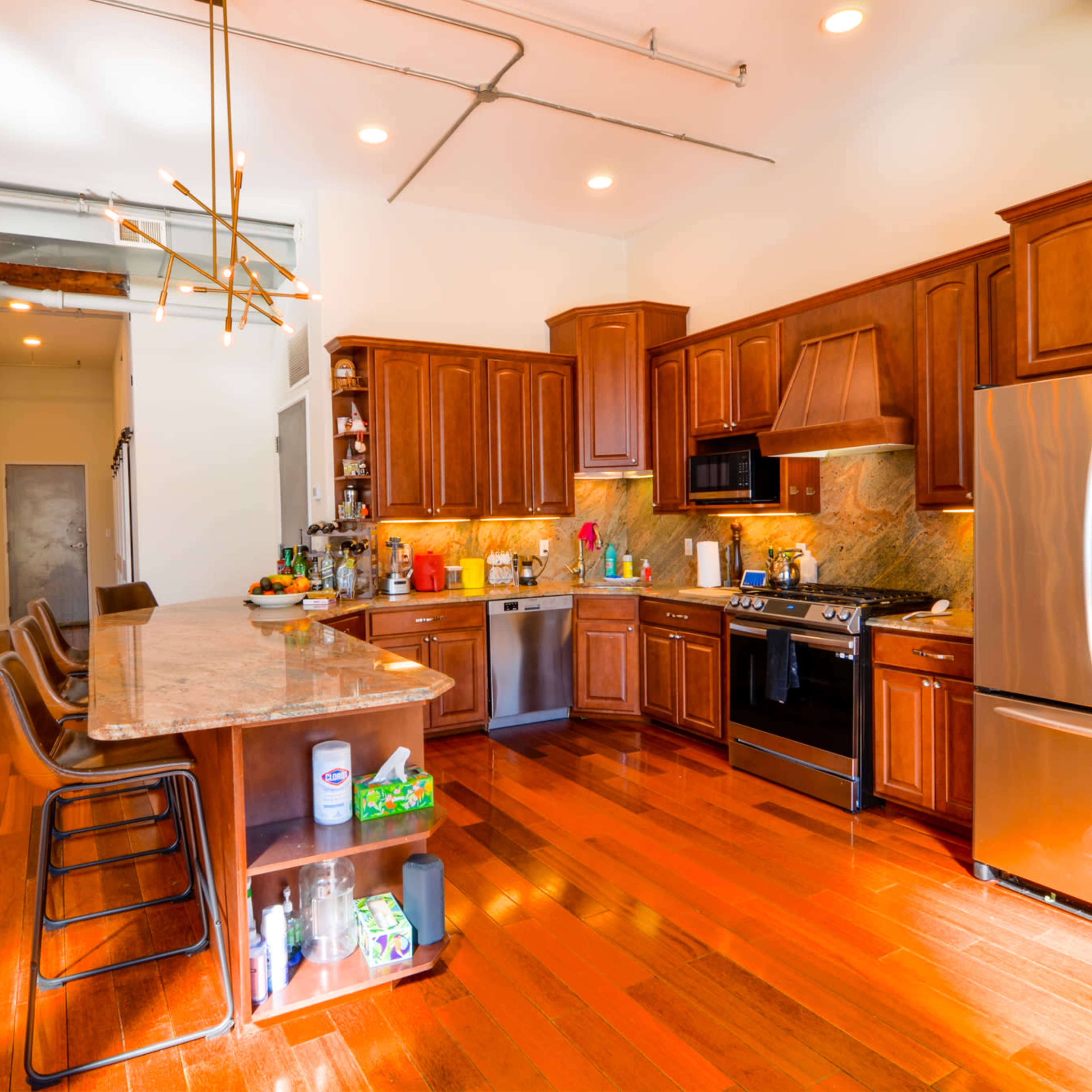 A modern kitchen with wooden cabinets, a granite countertop, stainless steel appliances, and hardwood flooring.