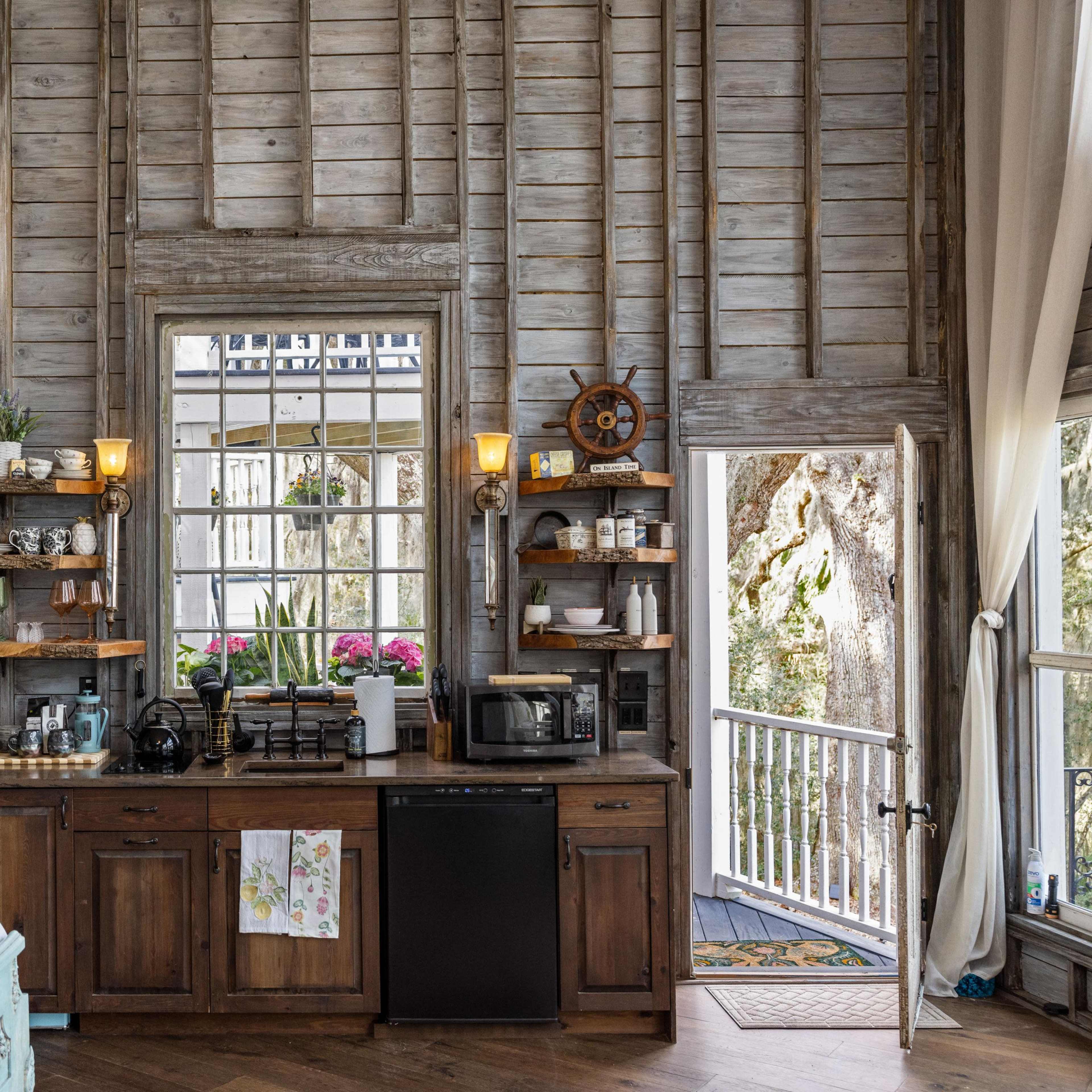 A rustic kitchen area with wooden shelves, a black refrigerator, and a large mirror, all within a cabin-style room featuring exposed wooden walls.
