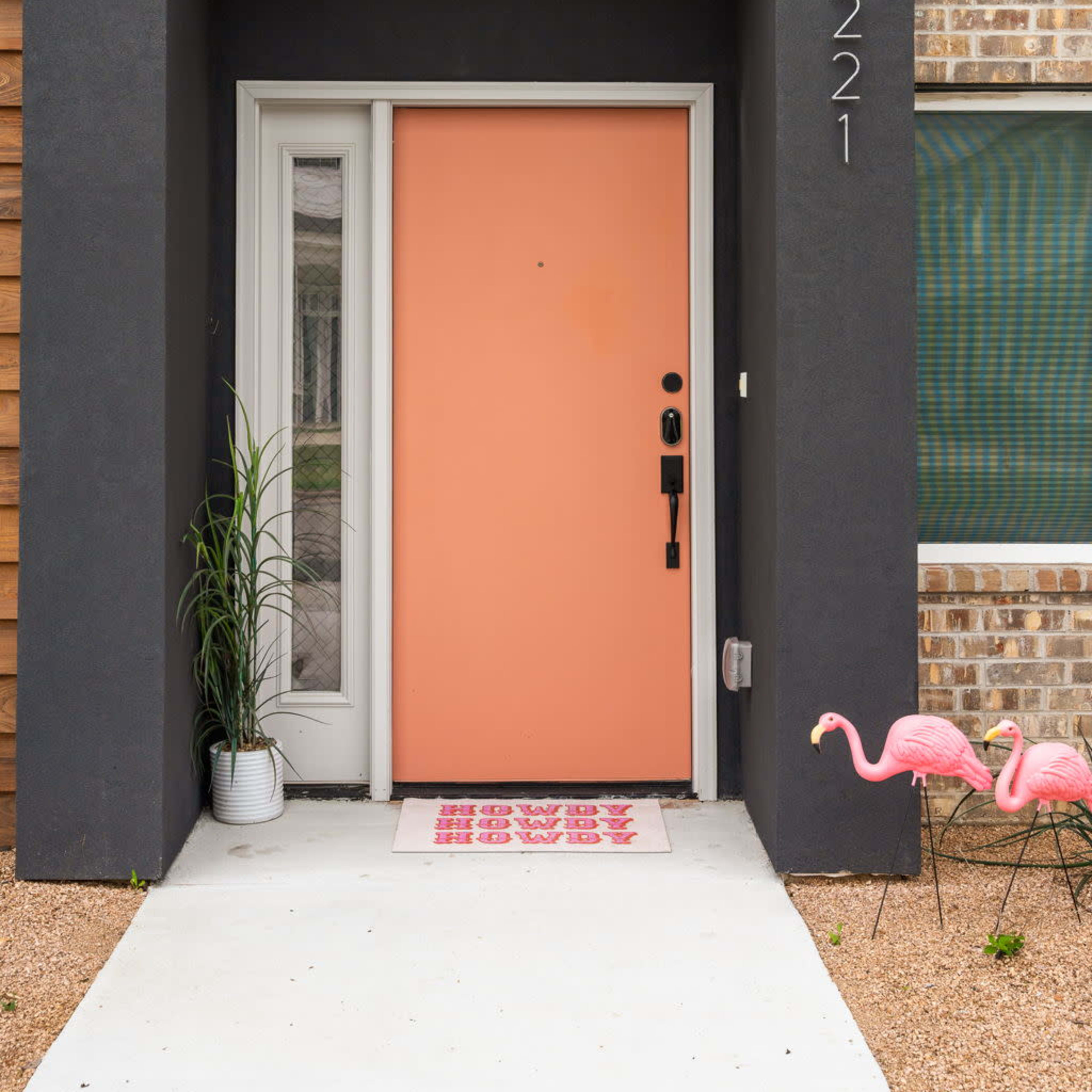 The entrance features a coral front door, flanked by a potted plant, with a welcome mat and two pink flamingo decorations outside.