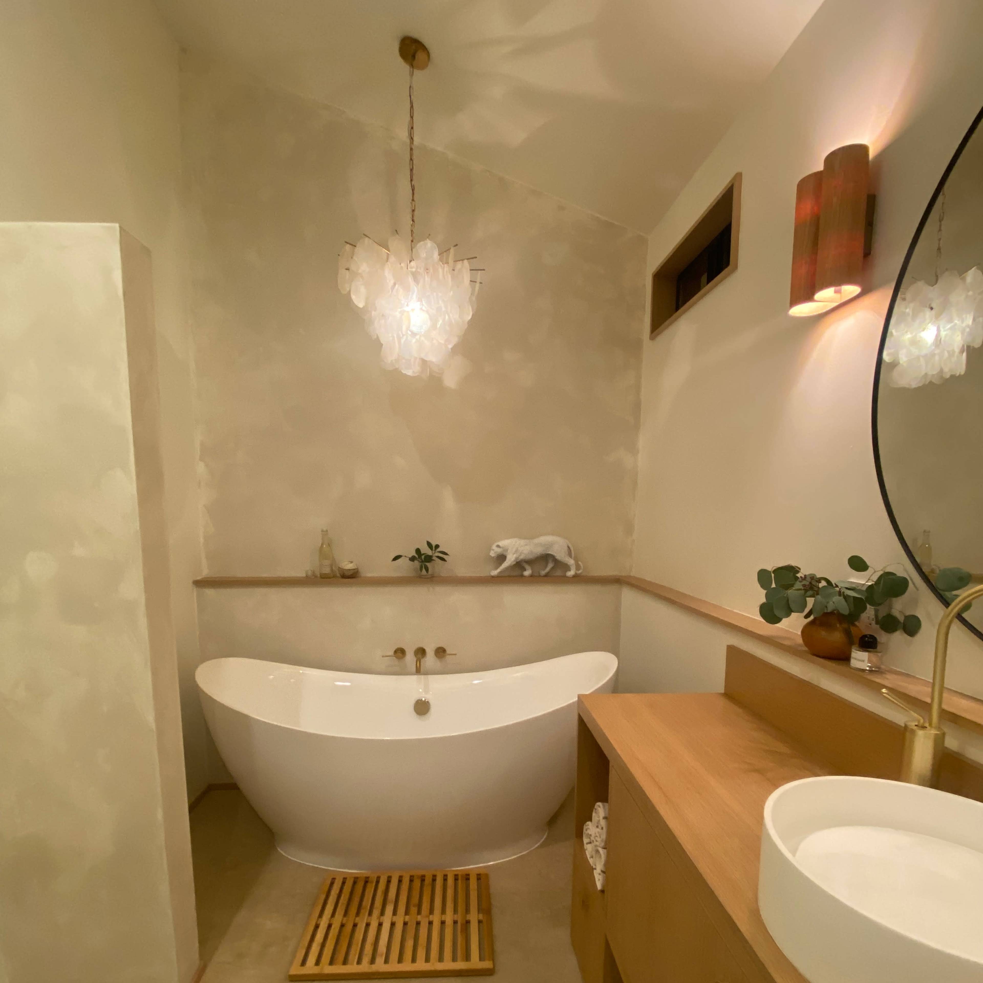 A modern bathroom featuring a freestanding white bathtub, a wooden vanity with a circular sink, and a pendant light above.