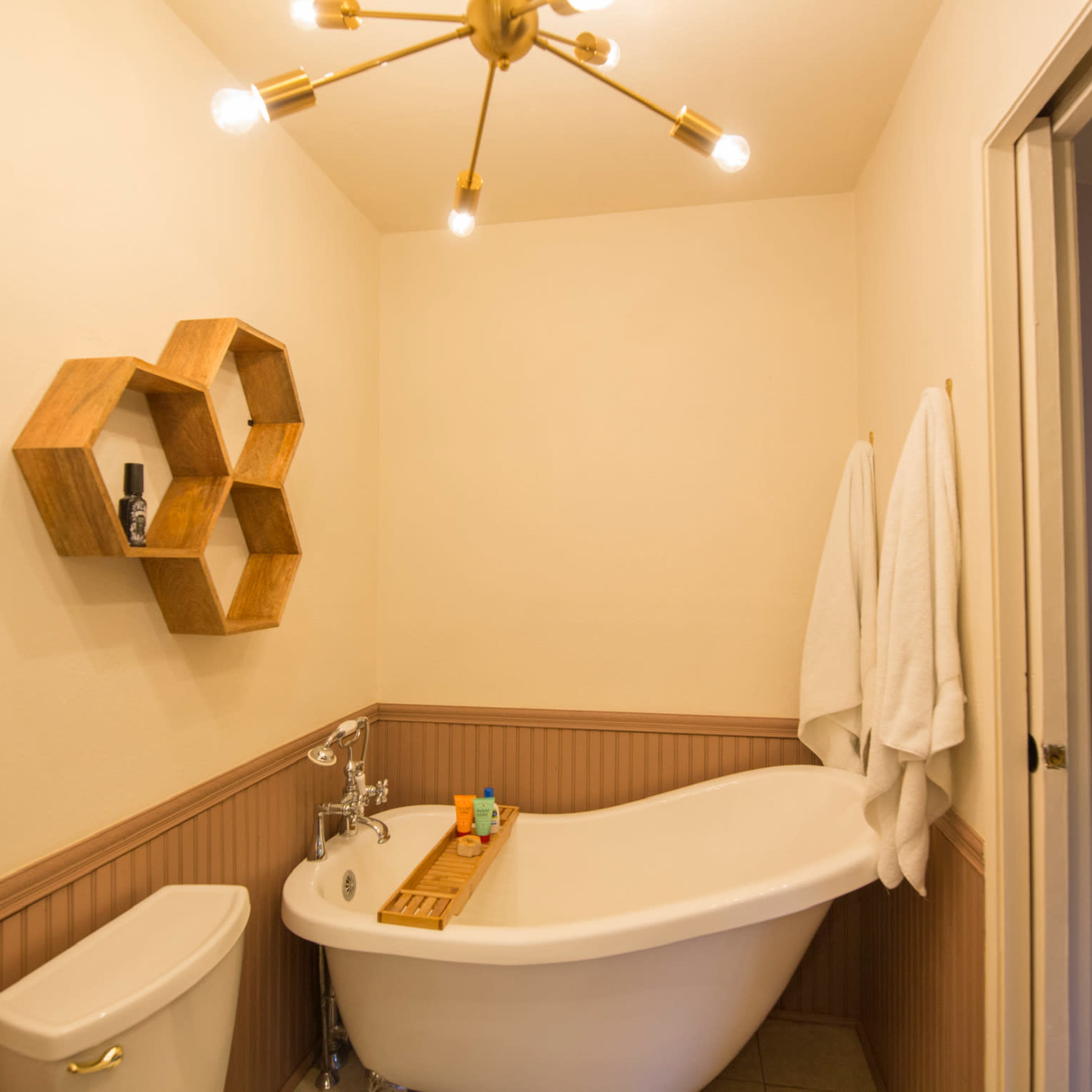 A bathroom featuring a freestanding bathtub, a wooden shelf with honeycomb design, and two white towels hanging on the wall.