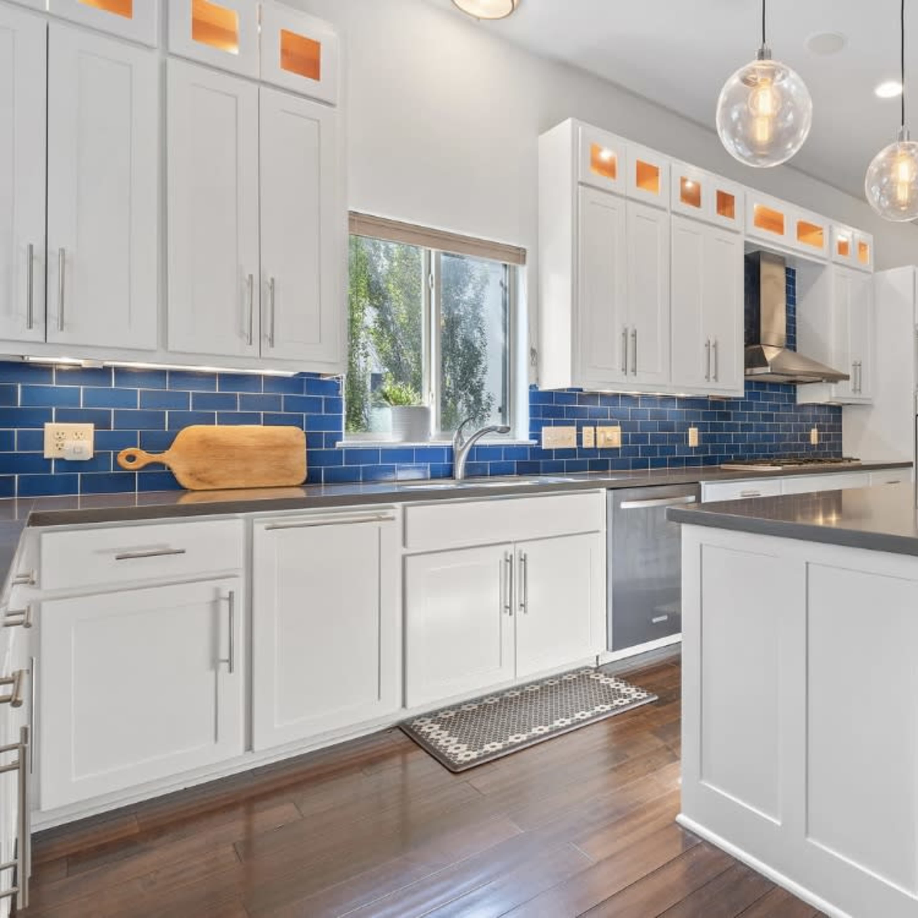 A modern kitchen featuring white cabinetry, a blue tiled backsplash, stainless steel appliances, and a central island with bar stools.