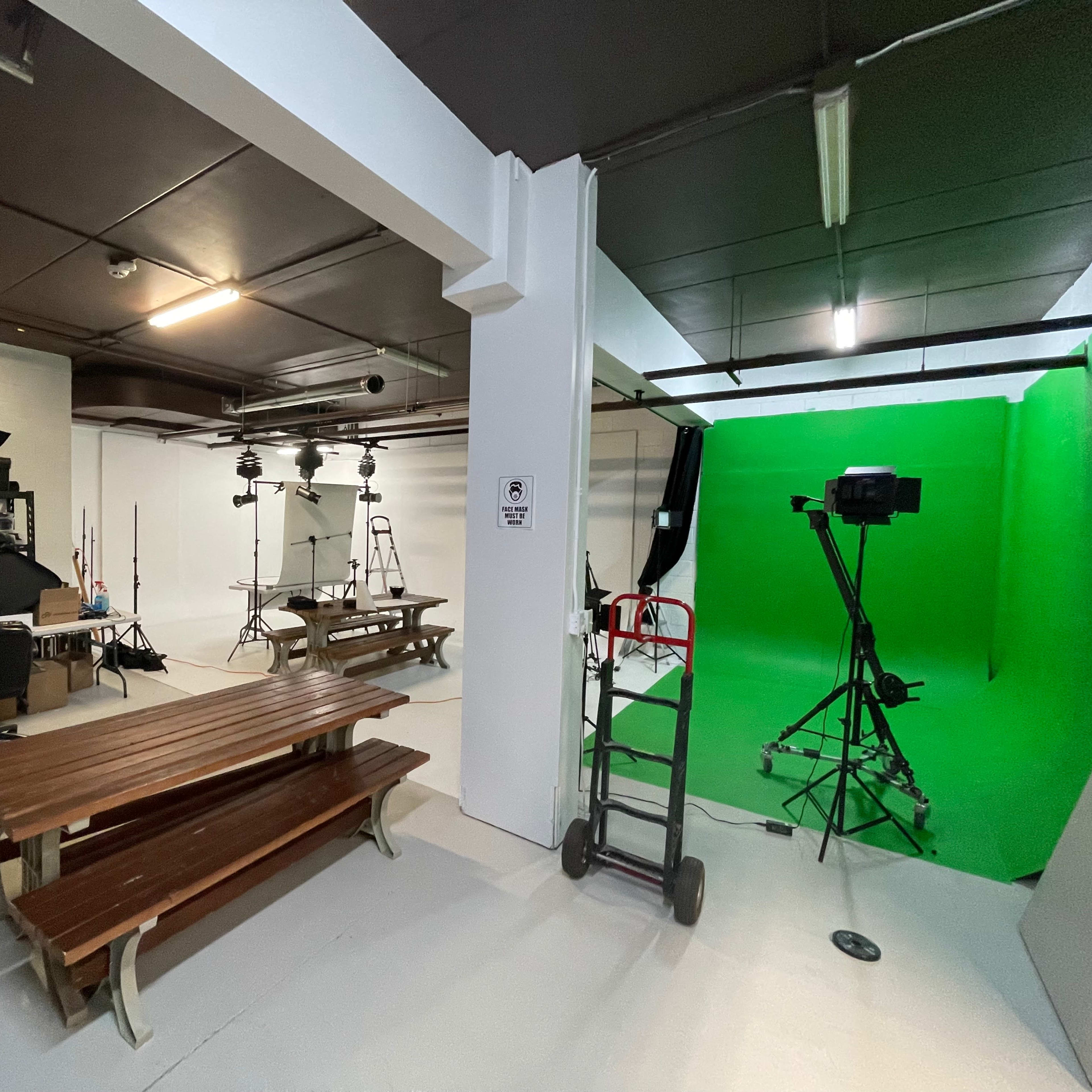 A spacious studio with a green screen setup, tables, lighting equipment, and various photography props neatly arranged on shelves.