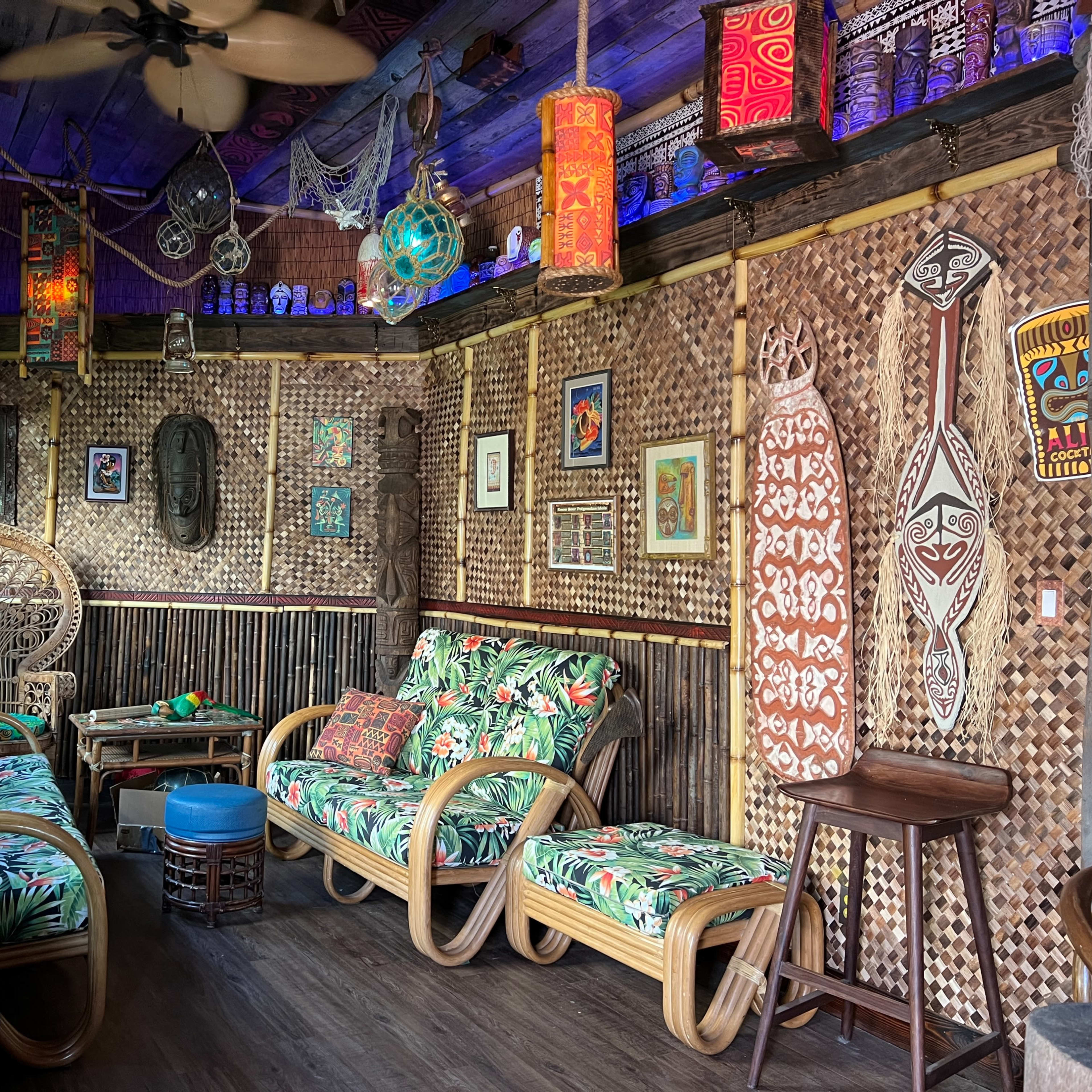A tropical-themed room with woven walls, patterned furniture, and decorative artifacts arranged around a seating area.