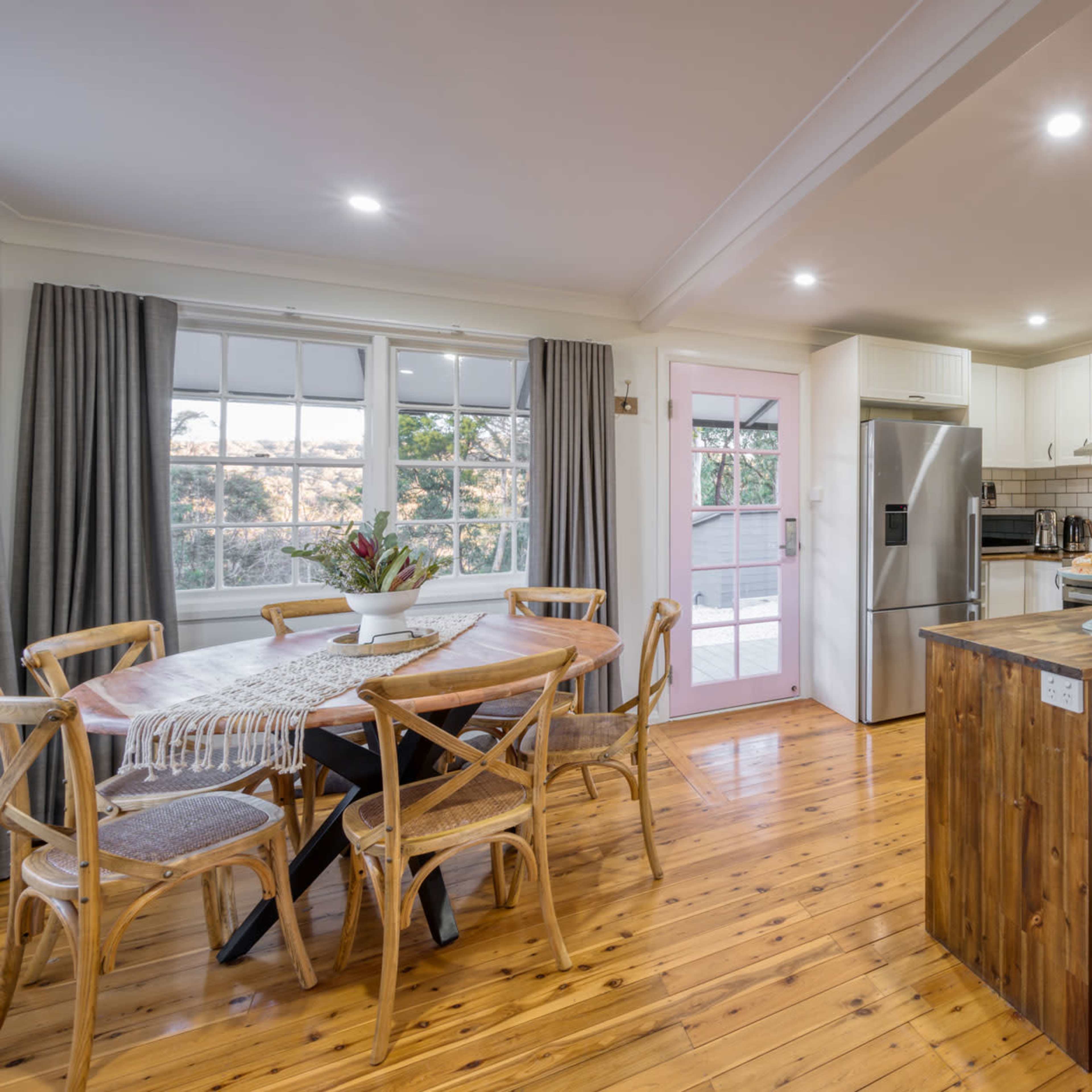 A modern kitchen and dining area with a wooden table, light-colored walls, and a large window providing natural light.