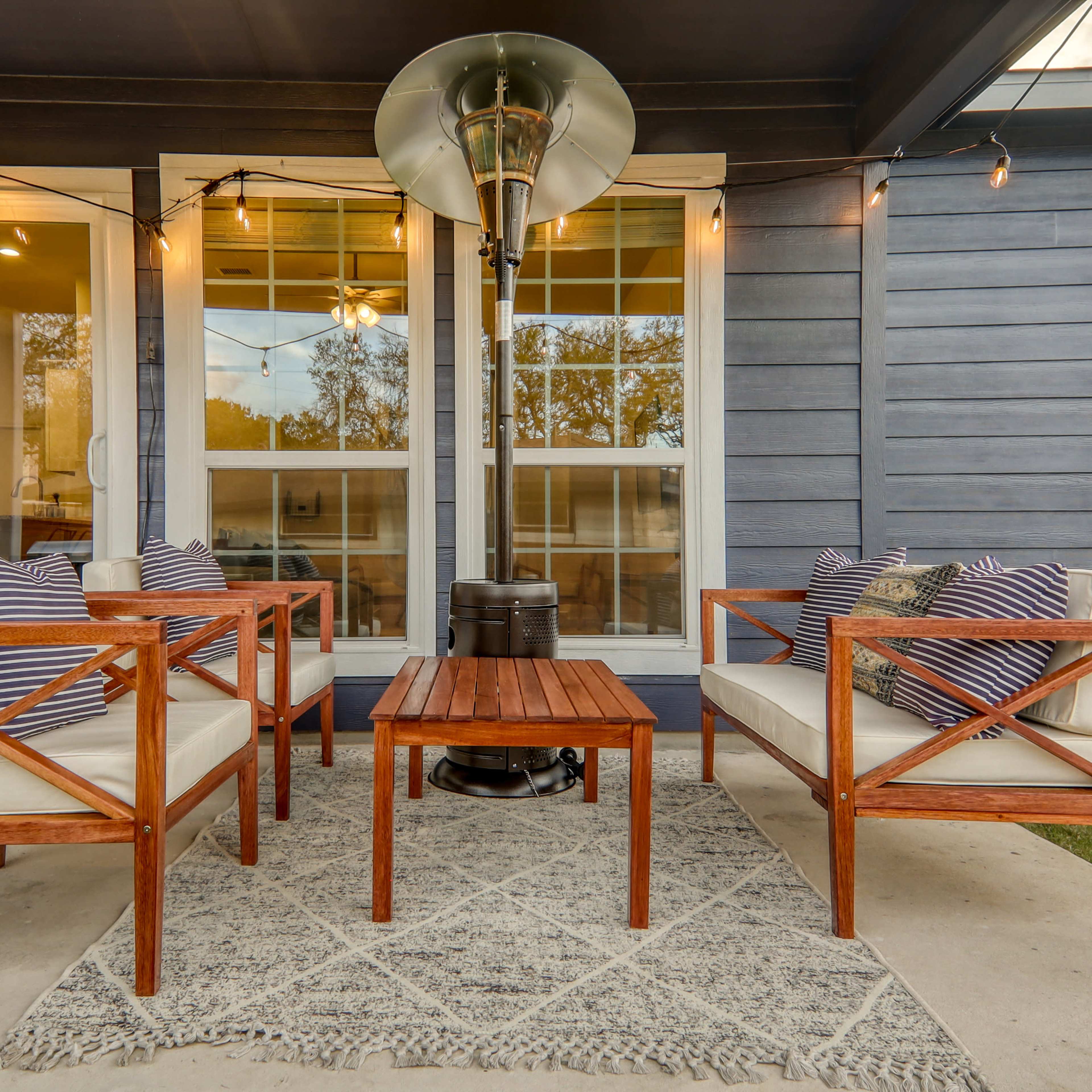 A cozy outdoor seating area with two wooden chairs, a small wooden table, and a patio heater, surrounded by string lights.