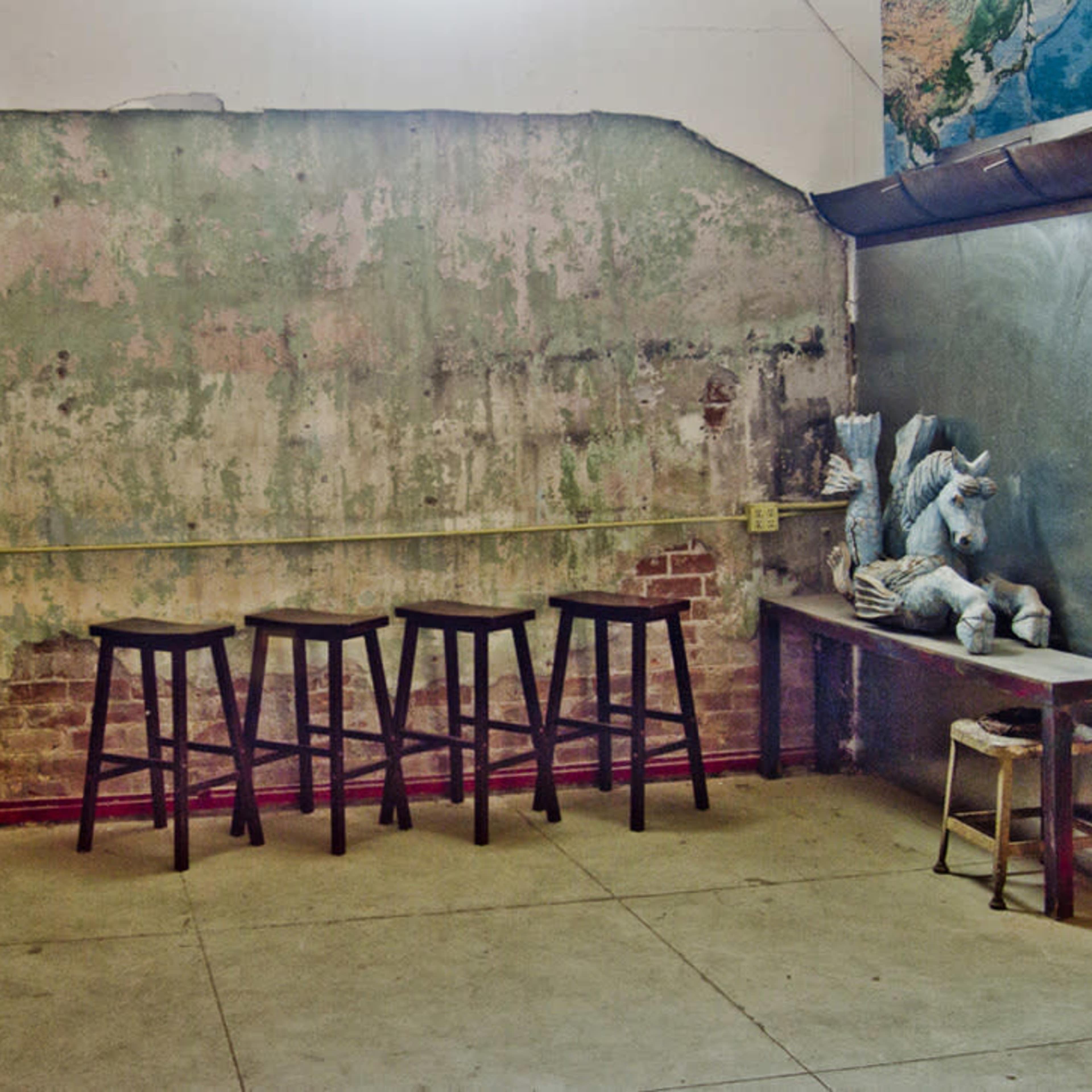 A sparse interior space with a textured wall, four black stools in a row, and a table with a sculpted figure on it.