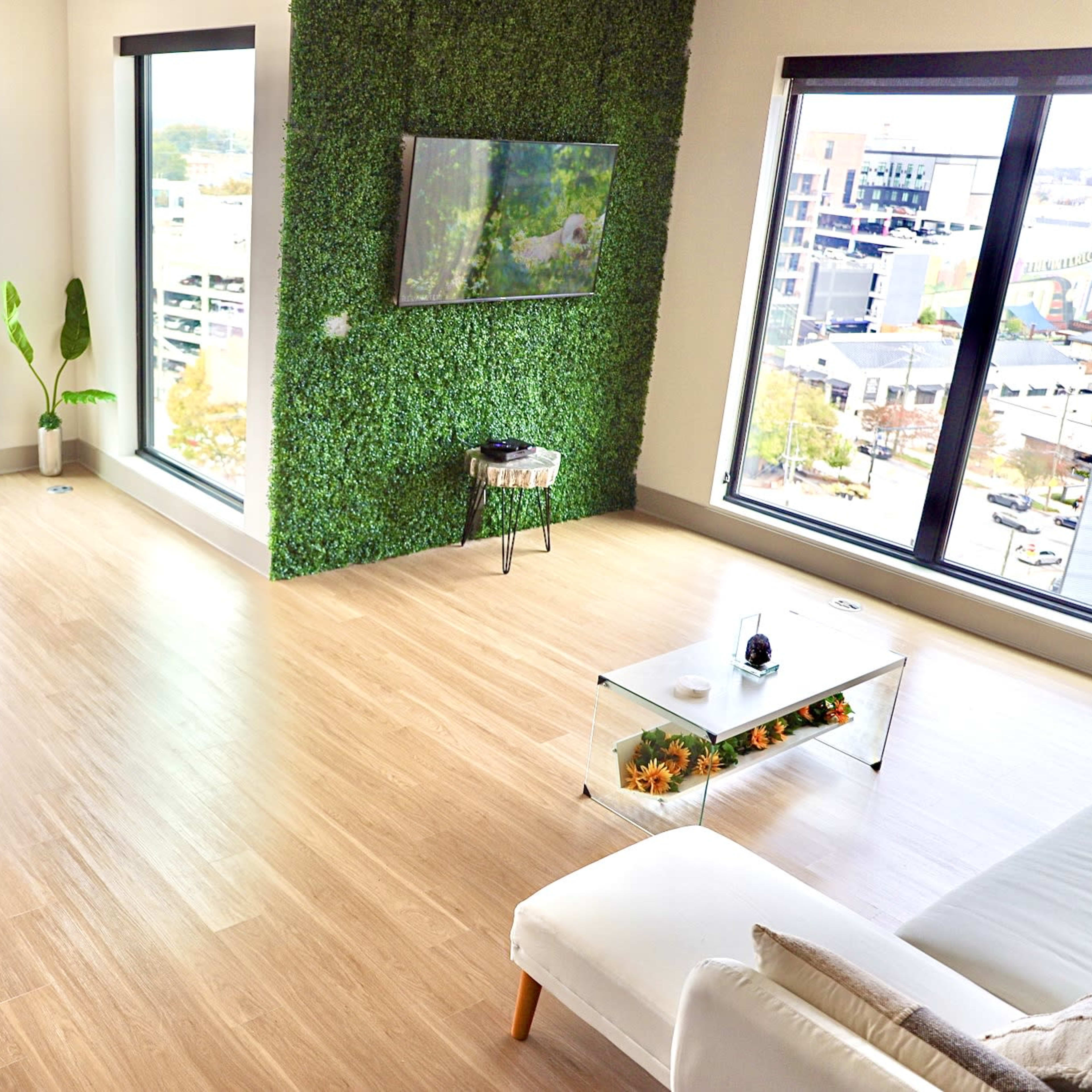A modern living space with large windows, a green wall, and a dining area featuring a table and chairs.