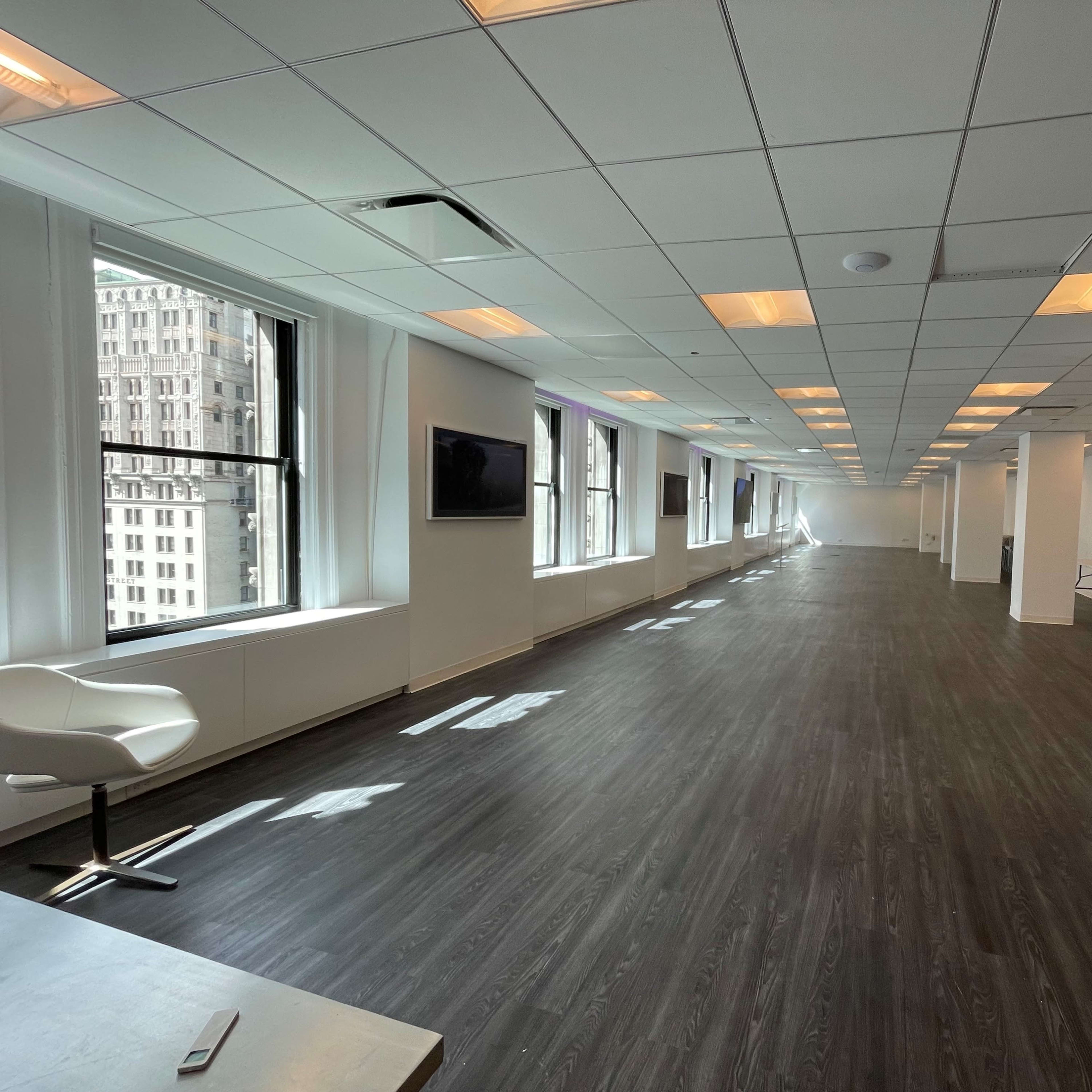 A spacious, modern office interior with large windows and polished wooden flooring.