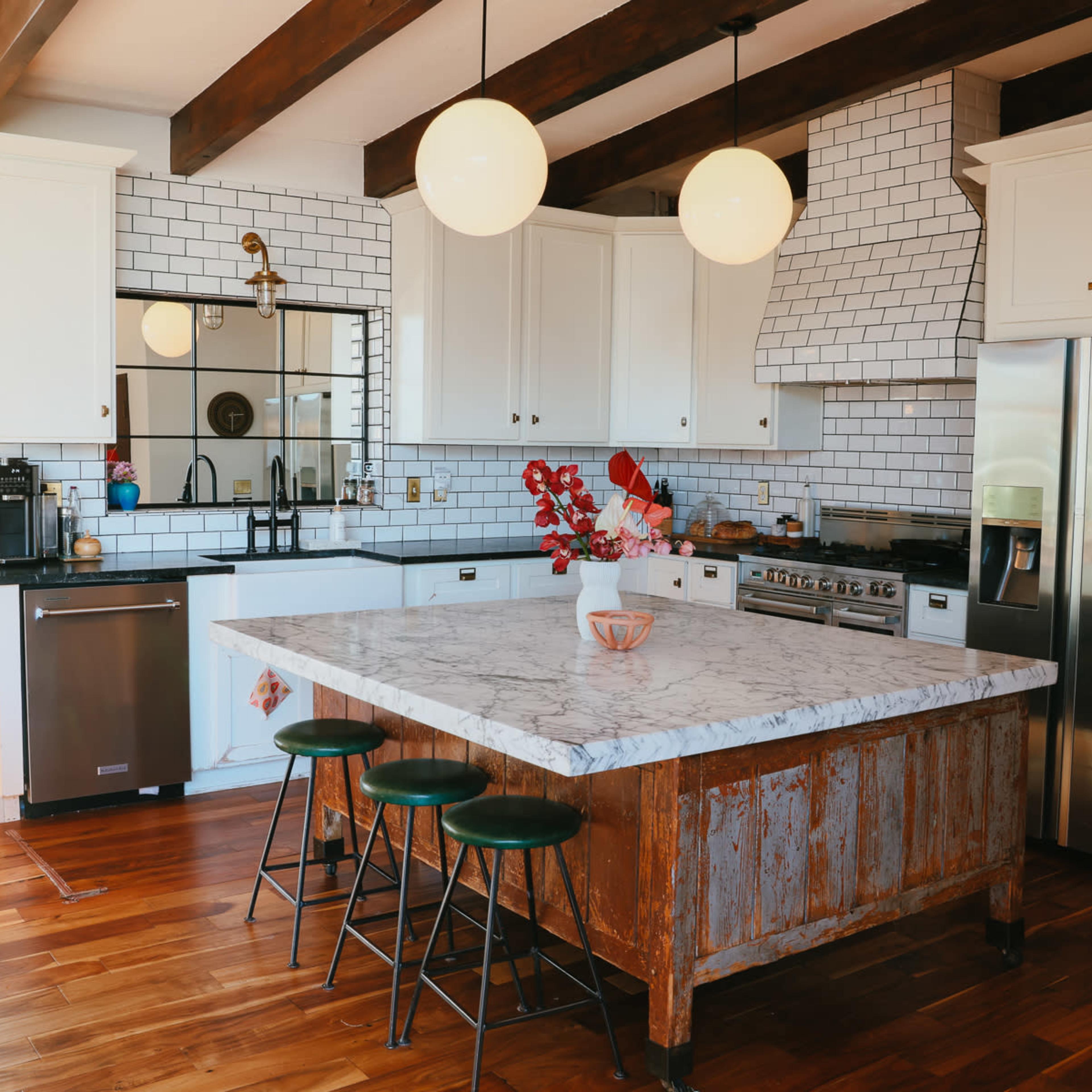 A modern kitchen features white cabinets, a marble-topped island with wooden accents, and stainless steel appliances.