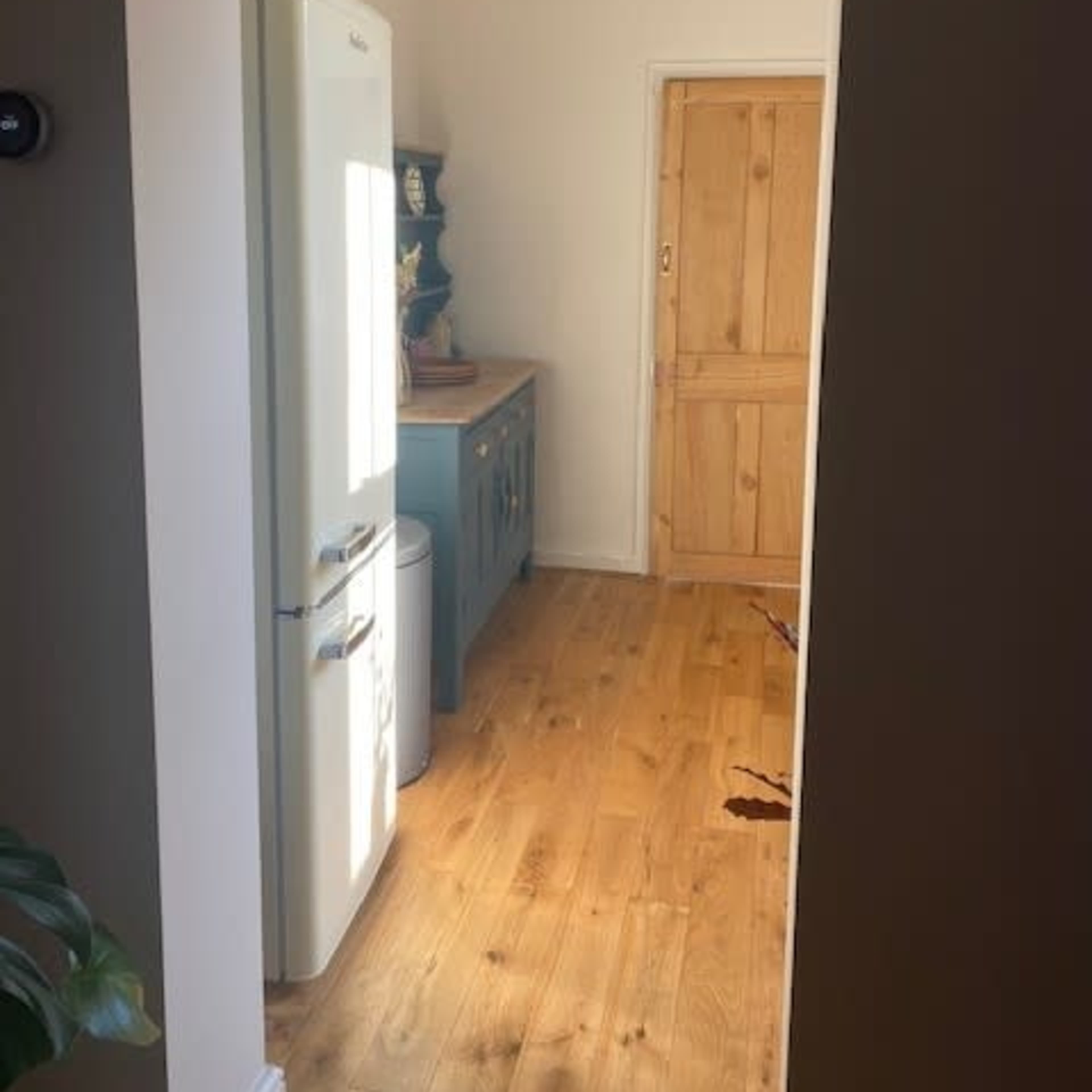 A narrow passage leading to a kitchen area with a white refrigerator, a wooden cabinet, and a wooden door.
