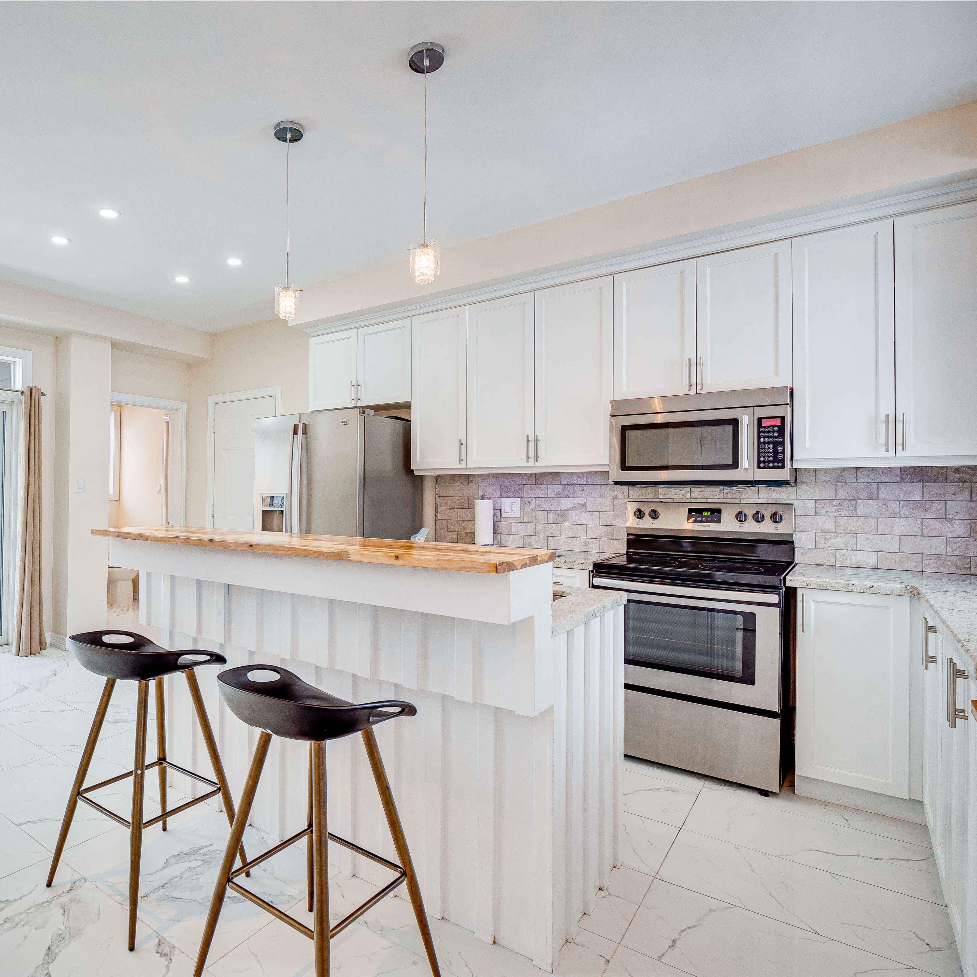 A modern kitchen features white cabinets, stainless steel appliances, and a central island with barstools, illuminated by pendant lights.