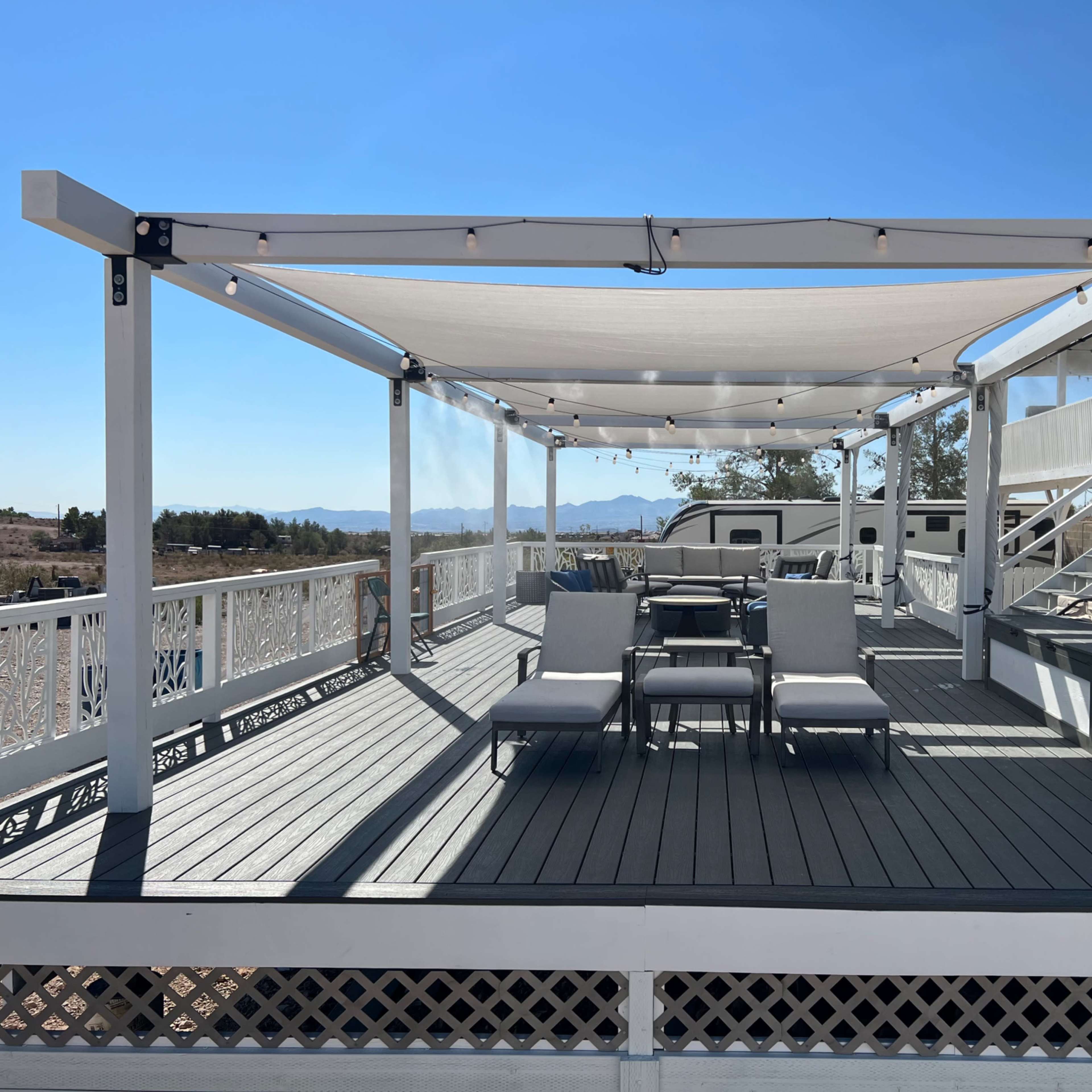 A spacious deck with a shaded seating area and a table, overlooking a landscape and mountains in the distance.