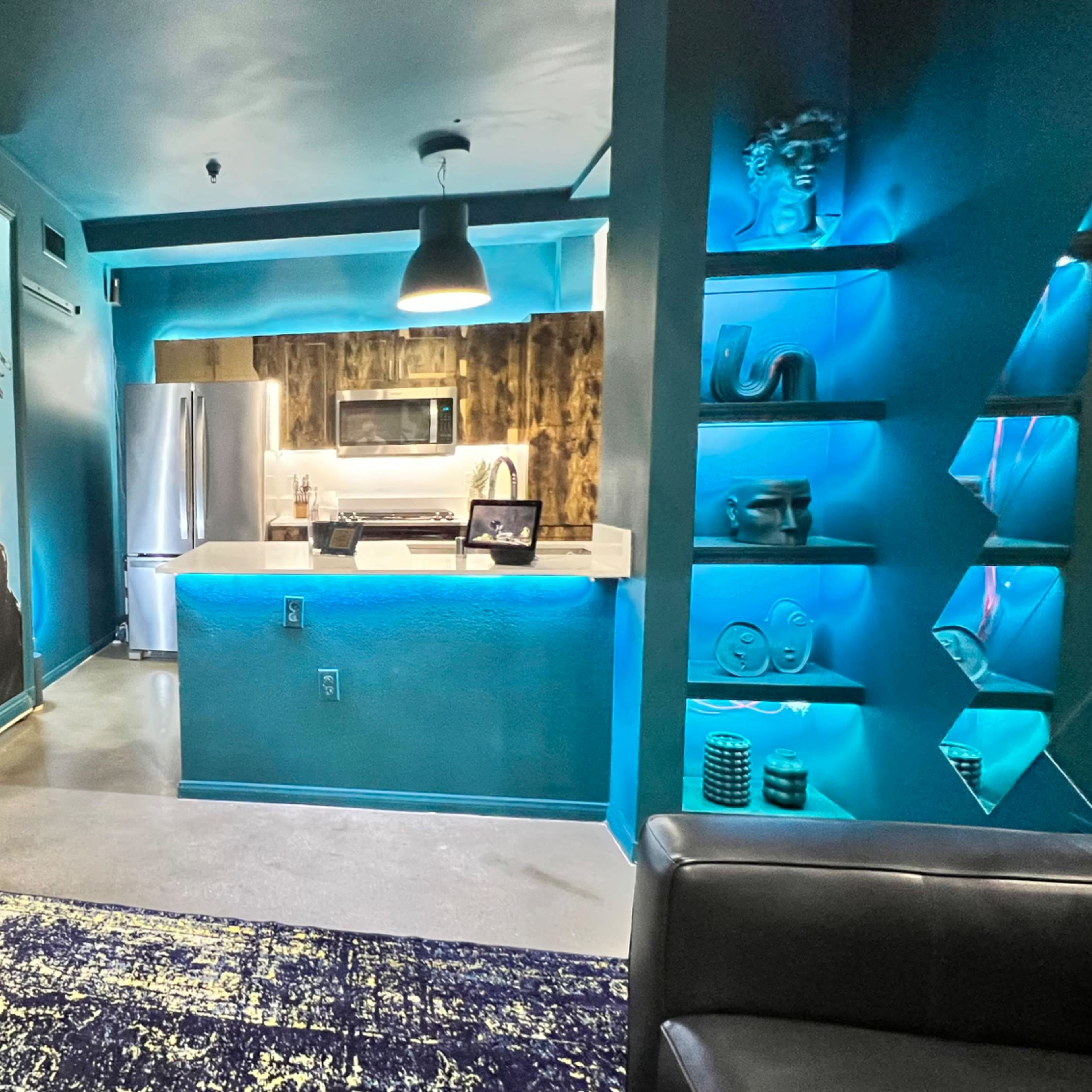 A modern living space with a vibrant mural on the wall, a kitchen area with stainless steel appliances, and blue accent lighting.