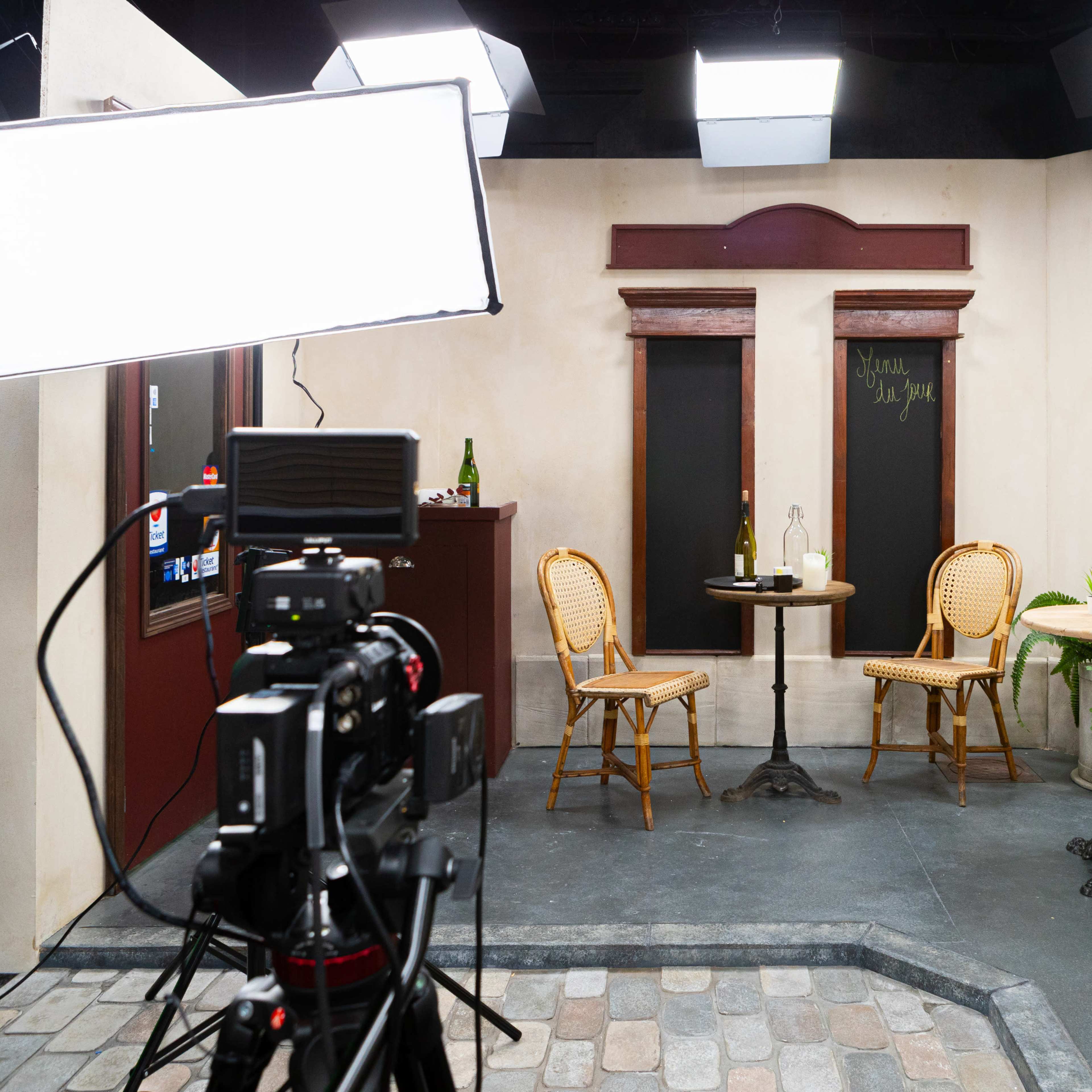 A small studio set with two bistro tables and chairs, a decorative wall fountain, and various lighting equipment.
